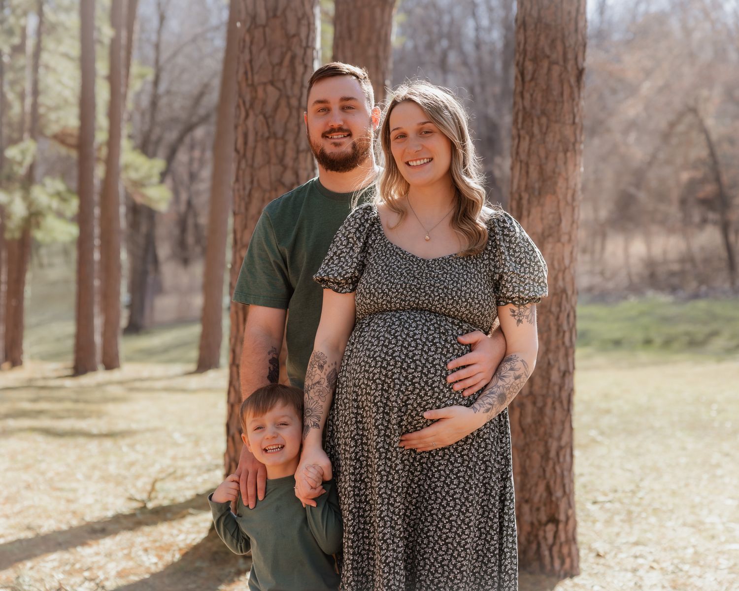 Outdoor family portrait in a pine forest featuring a maternity shoot and coordinated outfits.