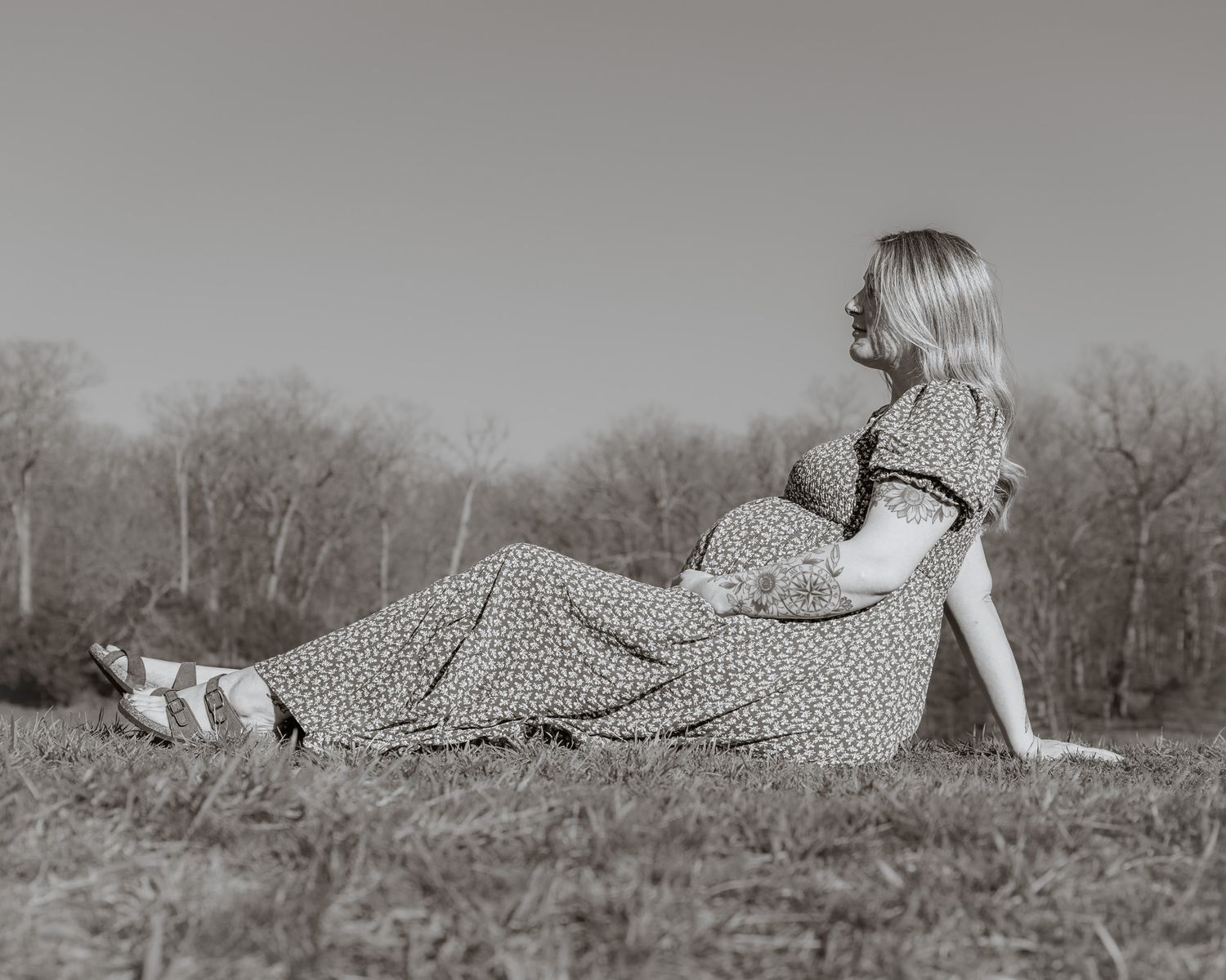Black and white portrait of woman in patterned dress reclining on grassy hillside.