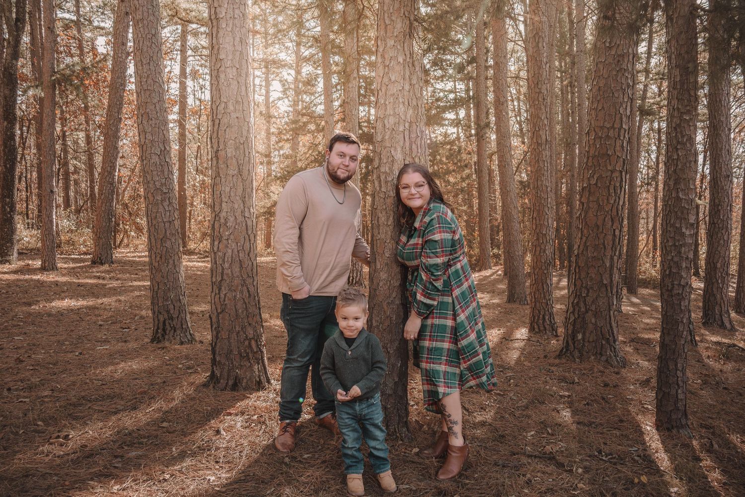 Family walks together through autumn forest with tall pine trees and golden sunlight filtering through branches.