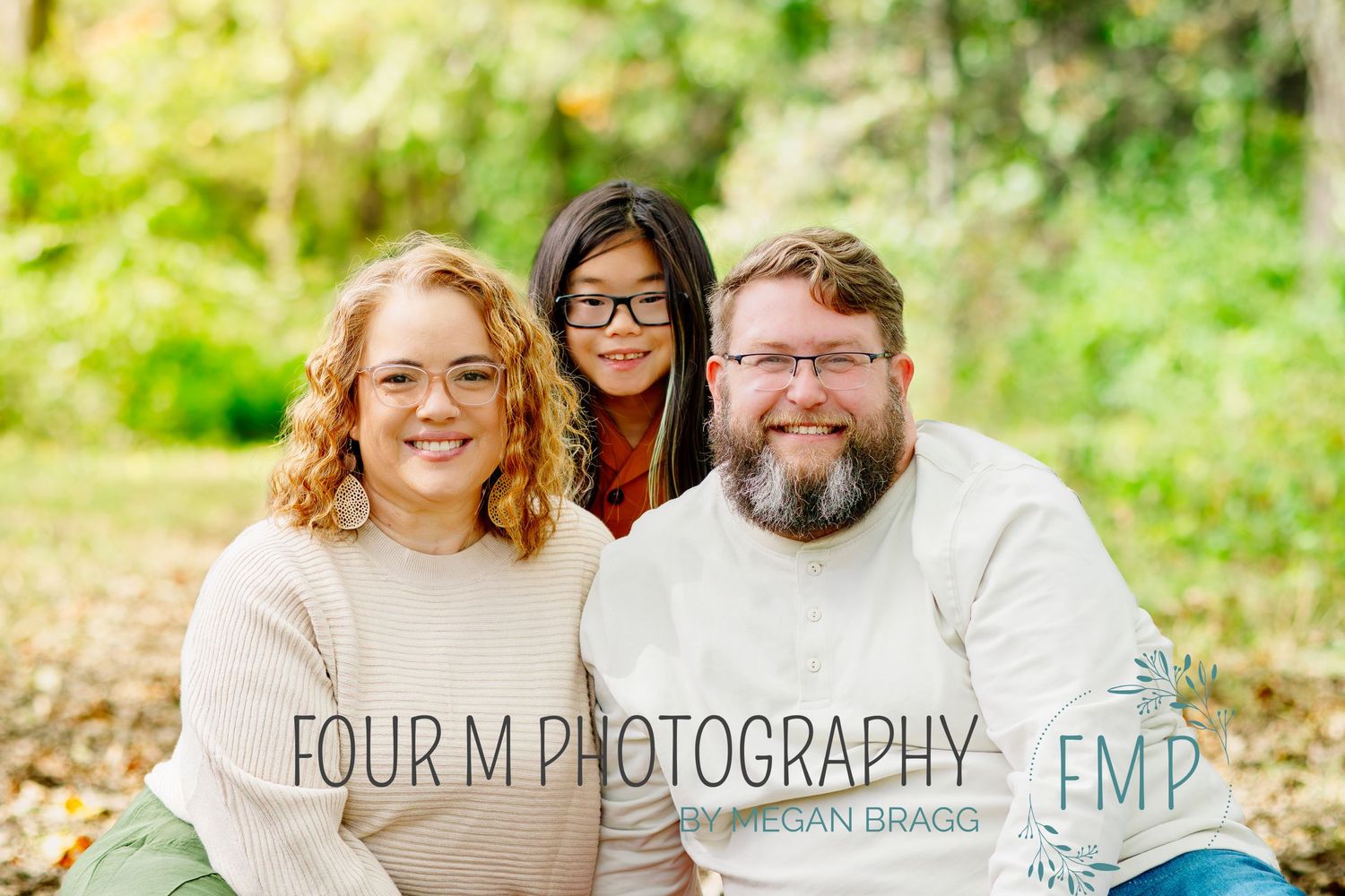 A cheerful family portrait taken outdoors with natural greenery in the background.