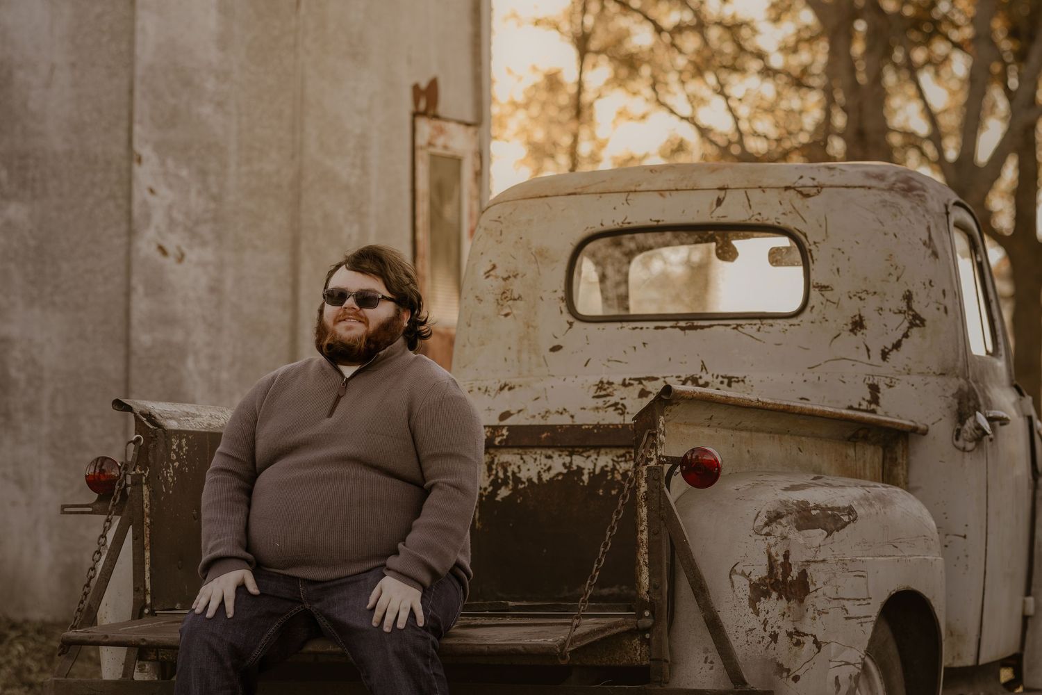 A vintage rustic pickup truck serves as a backdrop for an autumn portrait session at golden hour.