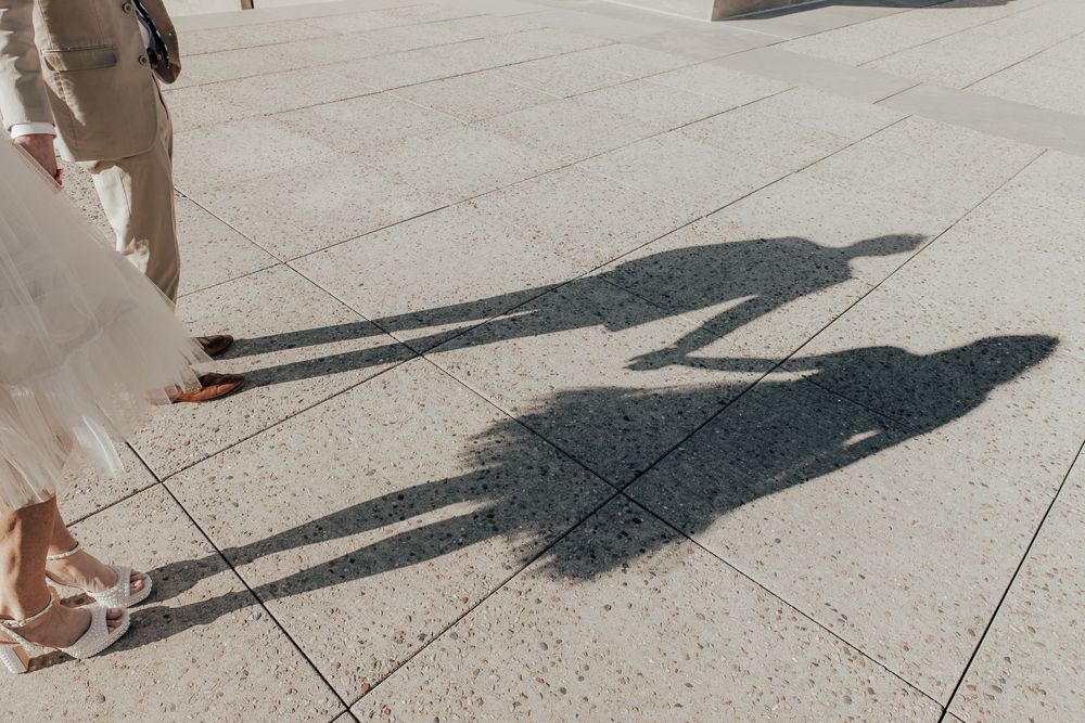 Long shadows of two people cast on concrete pavement during a sunny day.