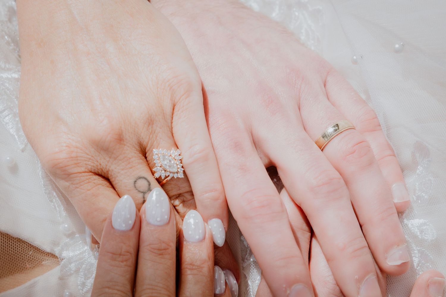 Close-up of bride and groom hands showing diamond engagement ring and wedding bands.