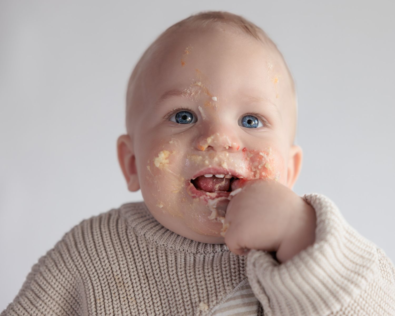 Adorable blue-eyed baby with cake smeared on face enjoying their first birthday smash cake.