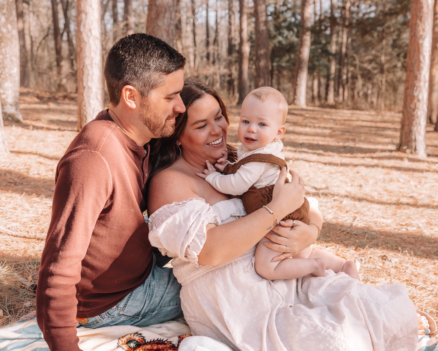 A family shares a tender moment together while sitting outdoors in a wooded setting during autumn.