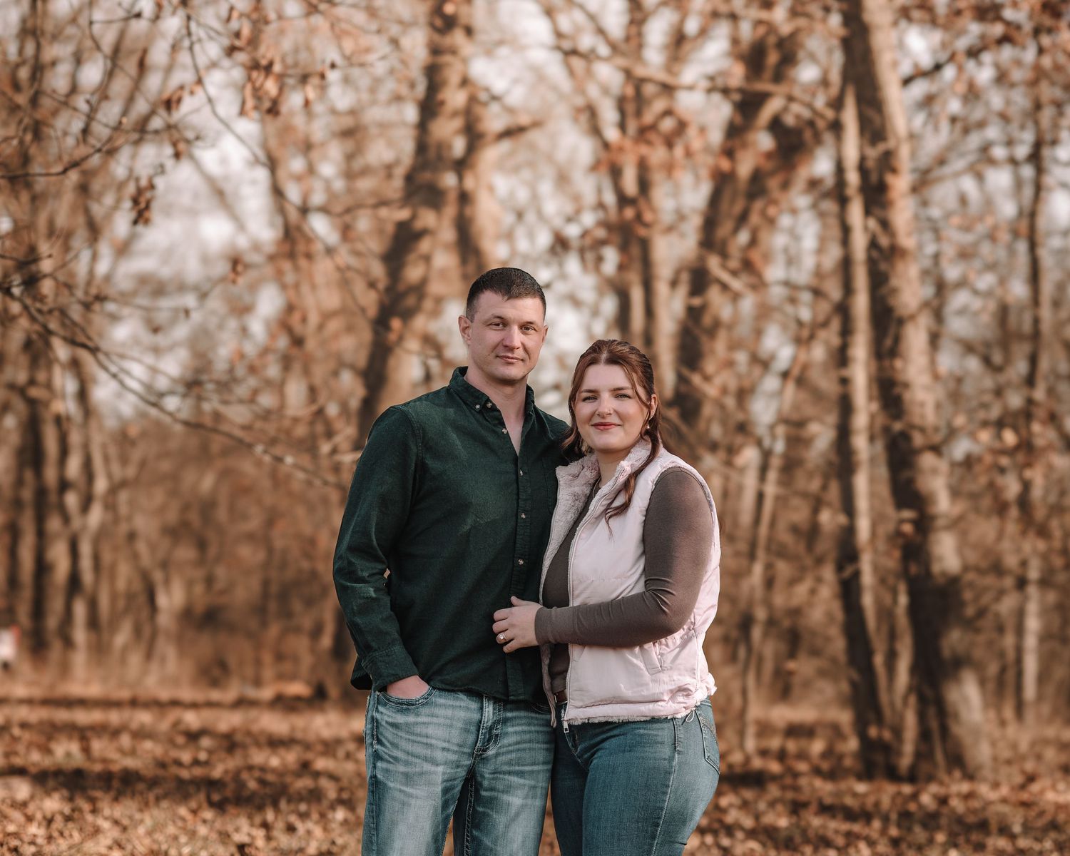 Couple embracing while standing among fall trees during an outdoor photo session.