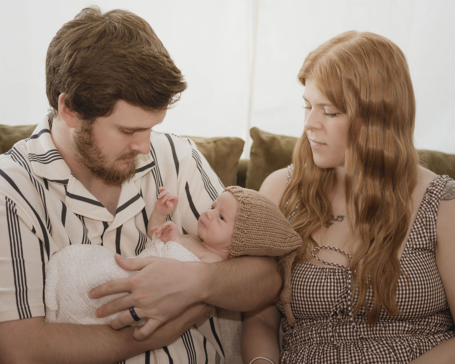 Young couple gazing lovingly at their newborn baby while seated on a couch.