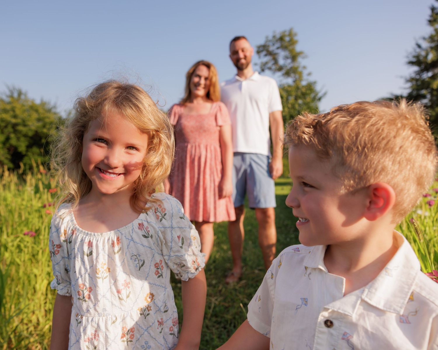 A happy family with two young children smiling in a sunny green field on a bright summer day.