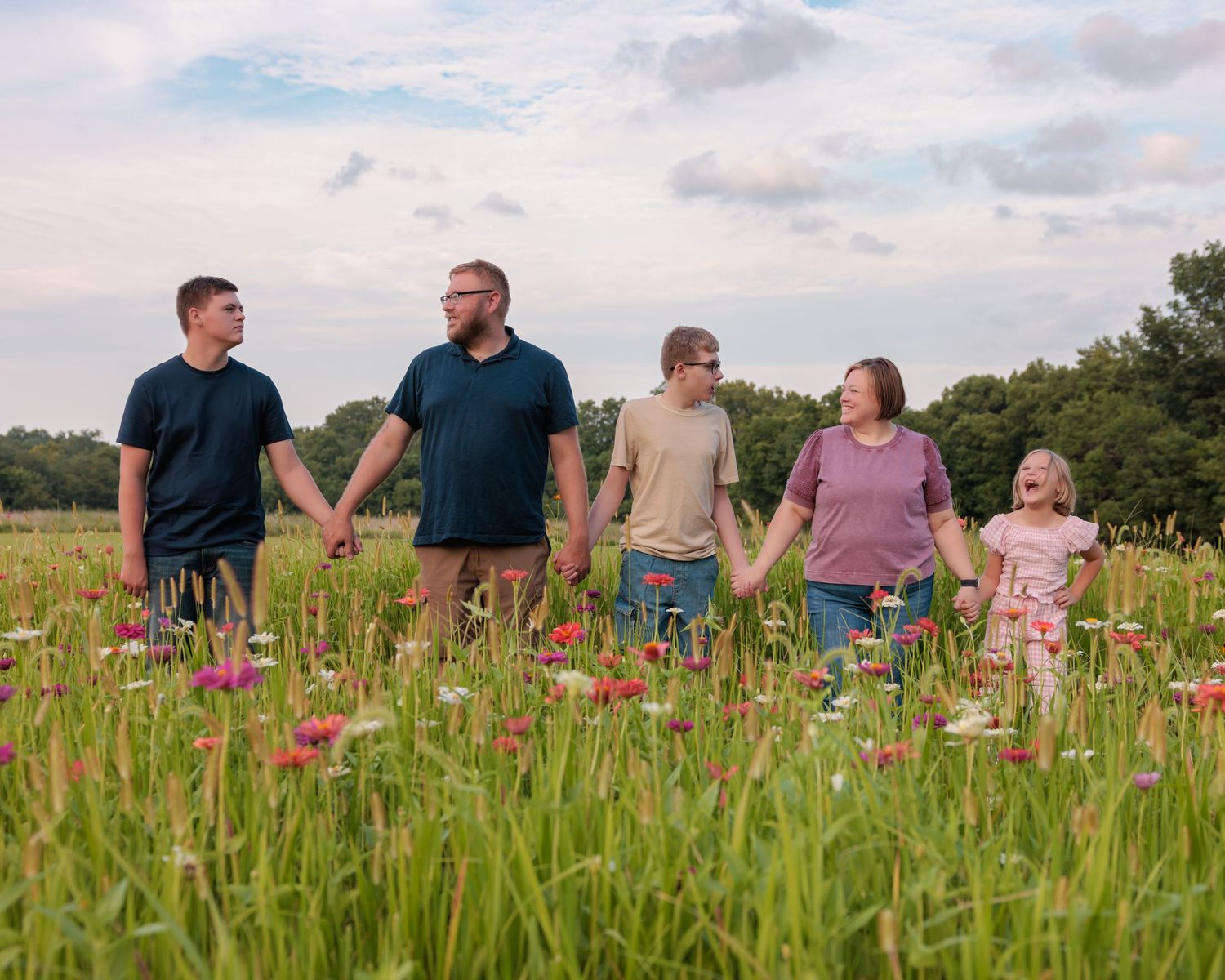 Family of five holding hands in a wildflower meadow under a cloudy sky.