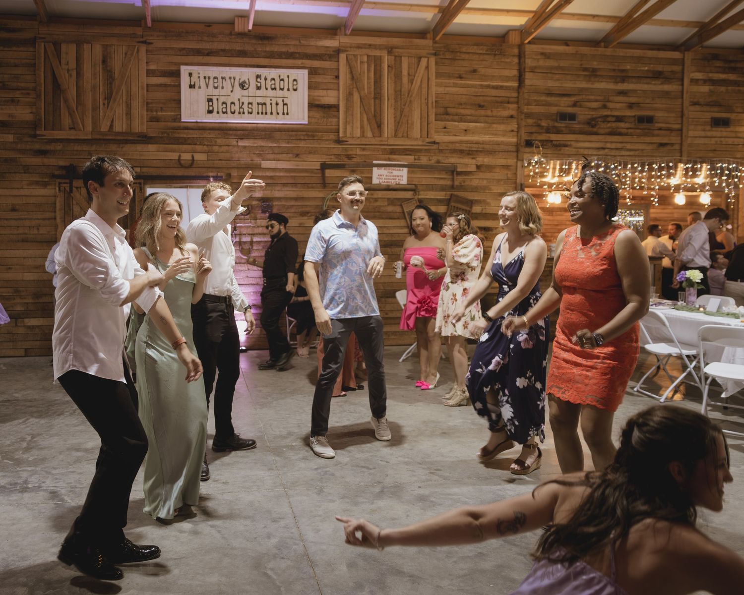 Guests dancing and celebrating at a rustic barn wedding reception with wood walls and string lights.