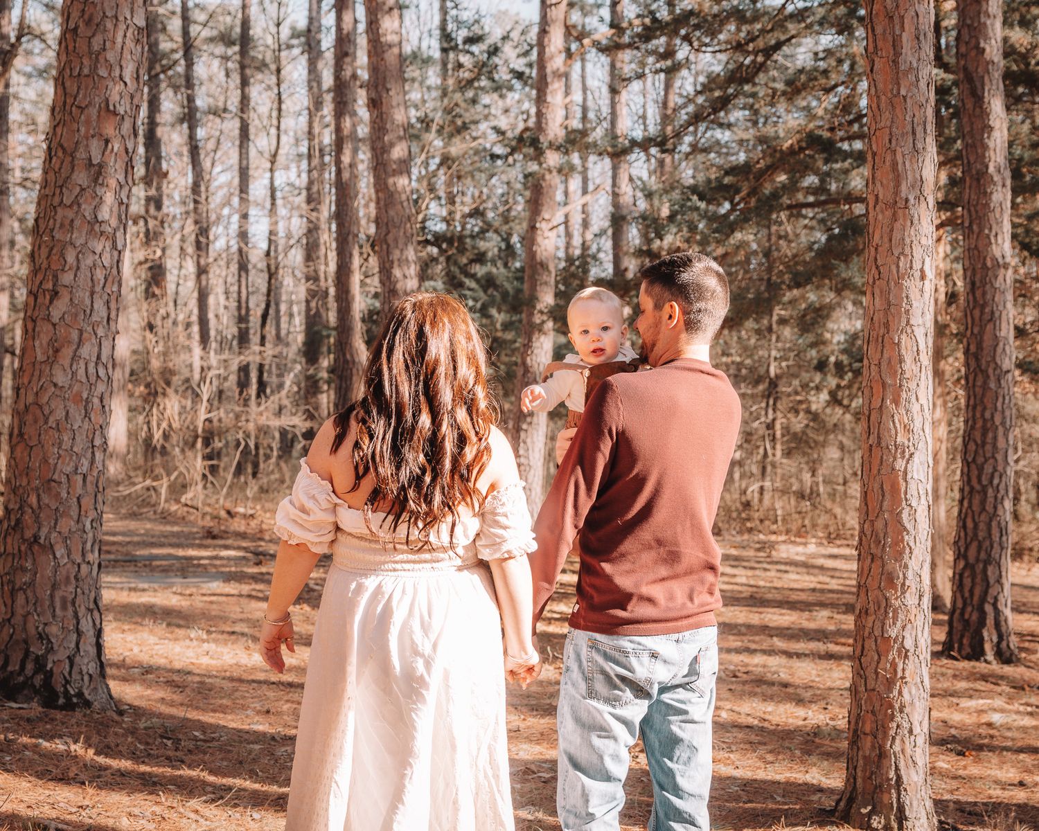 A family enjoys a tender moment together in a sunlit forest setting.