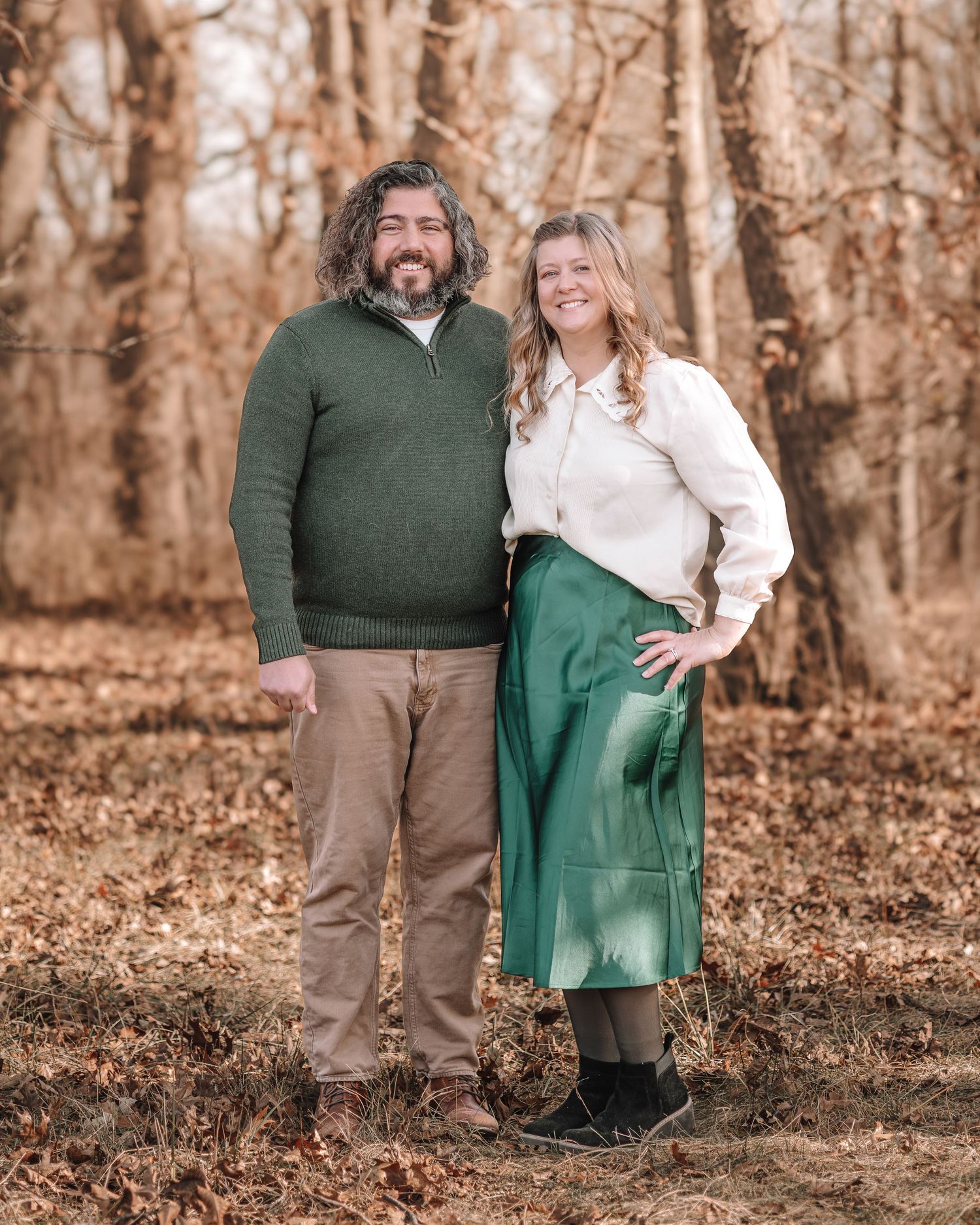 A couple posing together outdoors in coordinated green and white outfits among autumn trees.