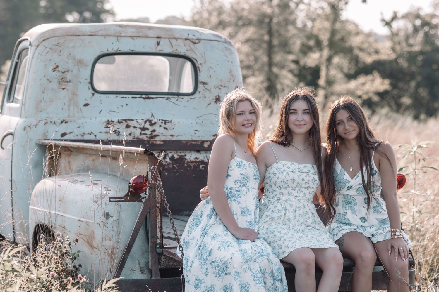 A group poses in front of a vintage blue pickup truck in a dreamy rustic outdoor setting during golden hour.