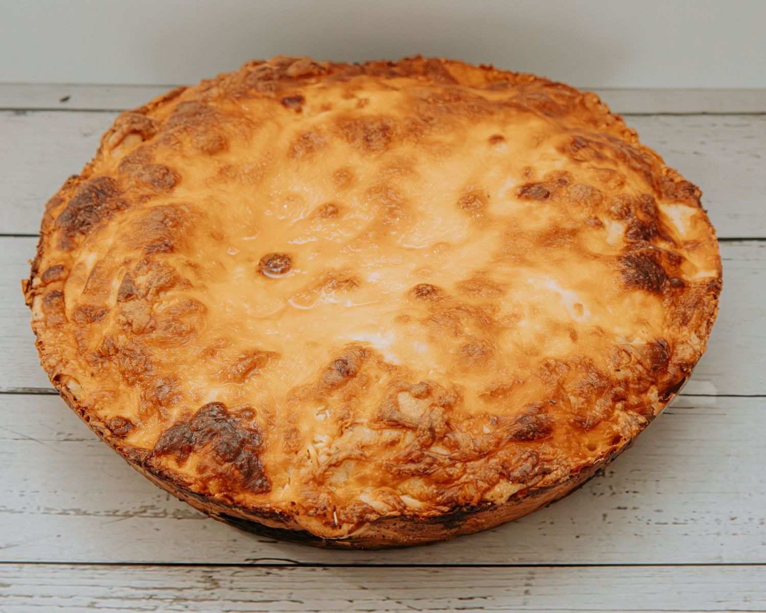 Freshly baked golden brown apple pie with flaky crust and bubbling filling on a rustic white wooden surface.