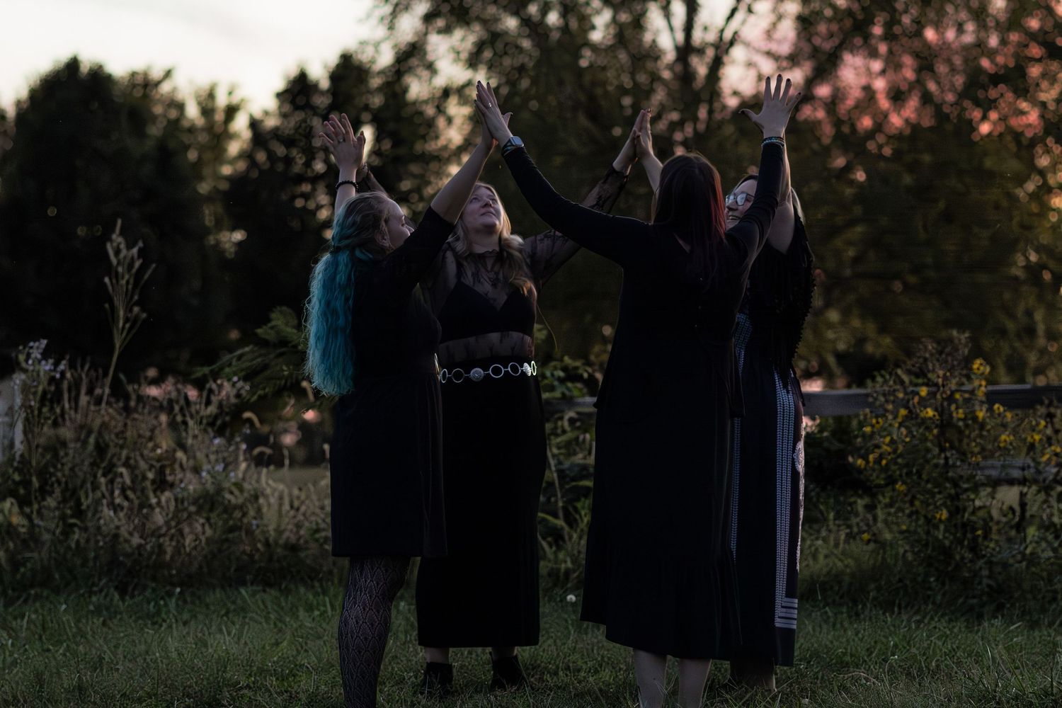 Silhouettes of people gathered outdoors during sunset with trees in the background.