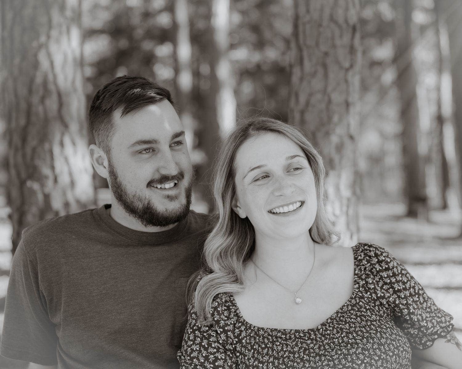 Black and white portrait of couple sharing genuine laughter in a wooded setting.