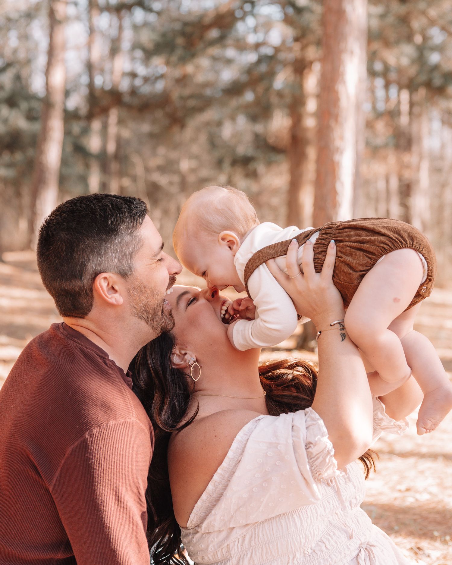 A romantic couple shares playful laughter while embracing in a sunlit forest setting.