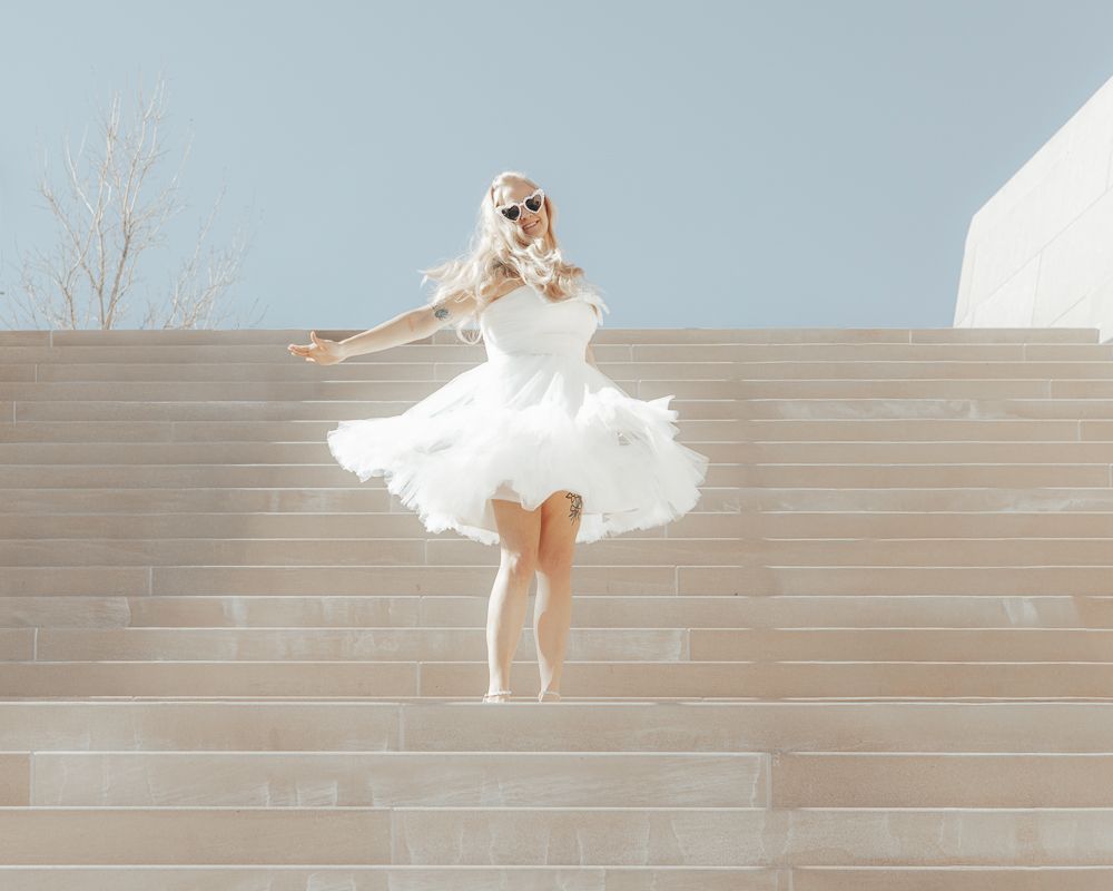 A dancer in a flowing white dress twirls gracefully across concrete steps in a series of dynamic poses.