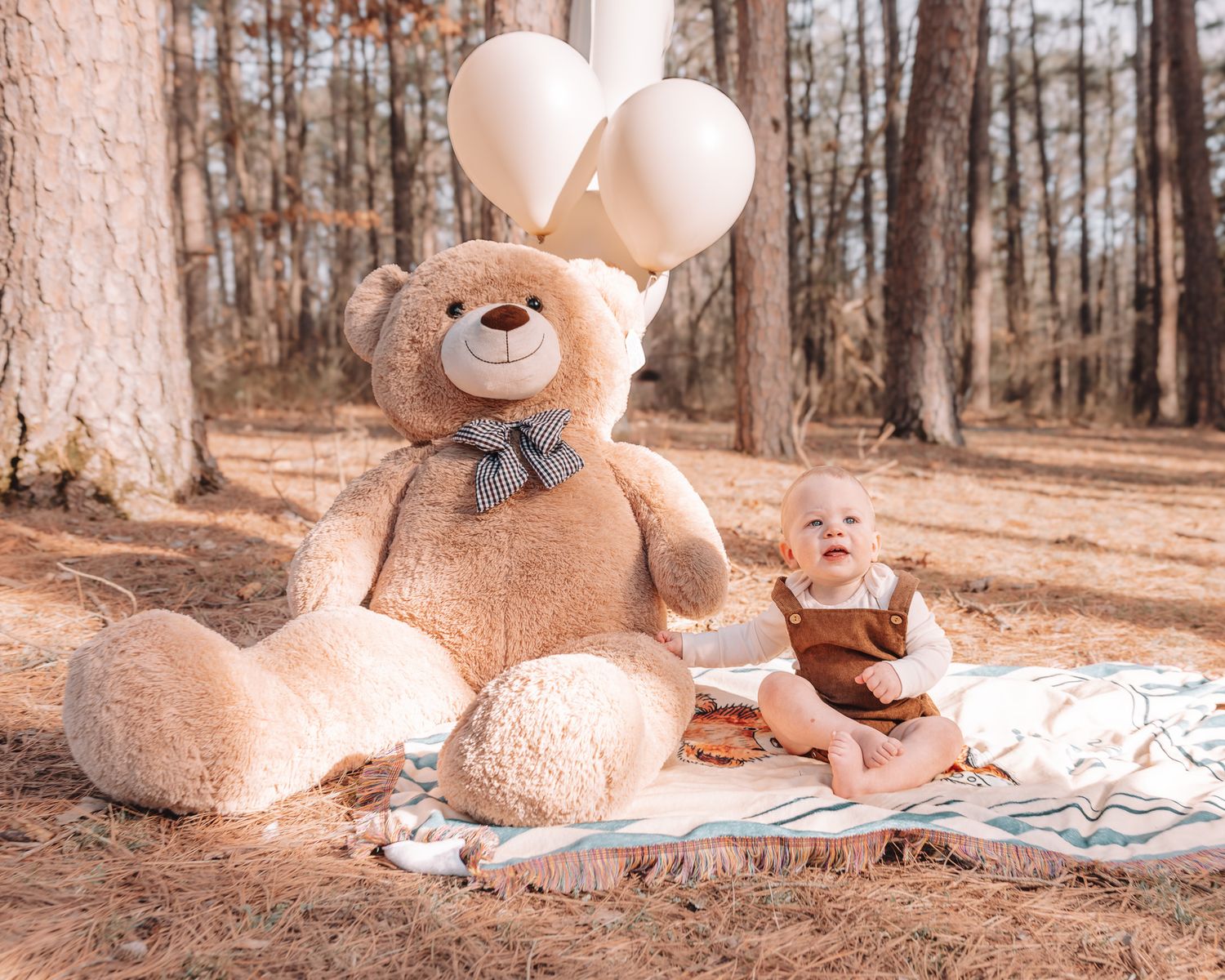A large teddy bear sits on a blanket in a wooded area during a sunny day.