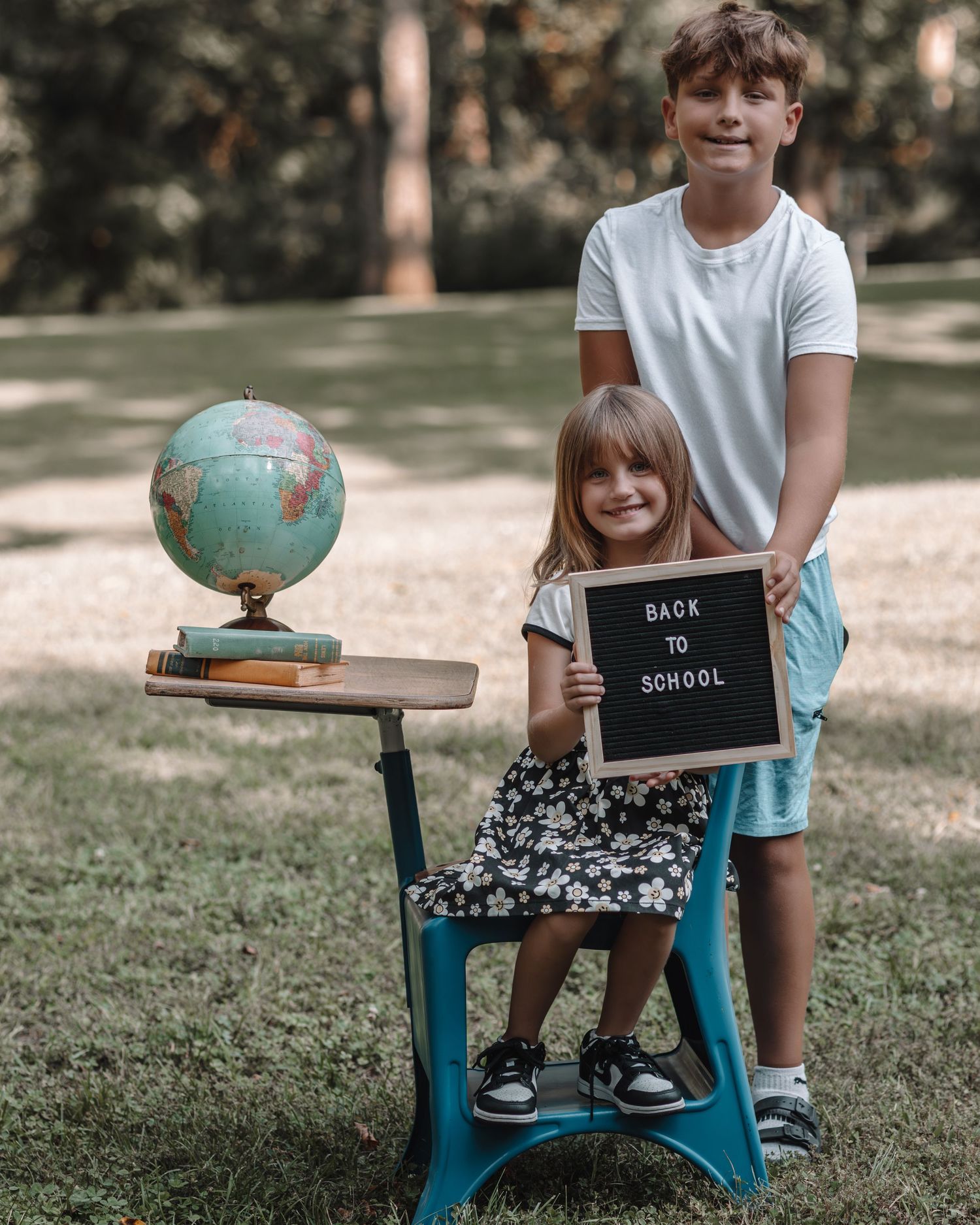 Vintage teal school desk with globe and chalkboard sign photographed outdoors in a park setting.