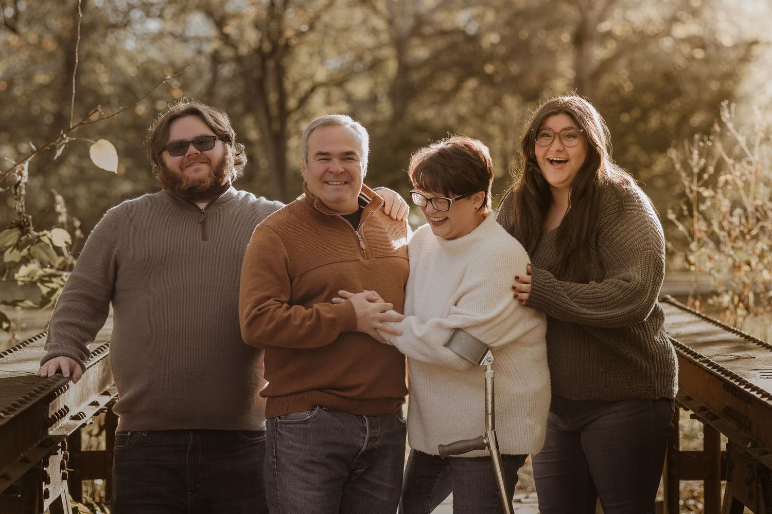 Candid family moment captured on rustic wooden bridge with autumn foliage in background.