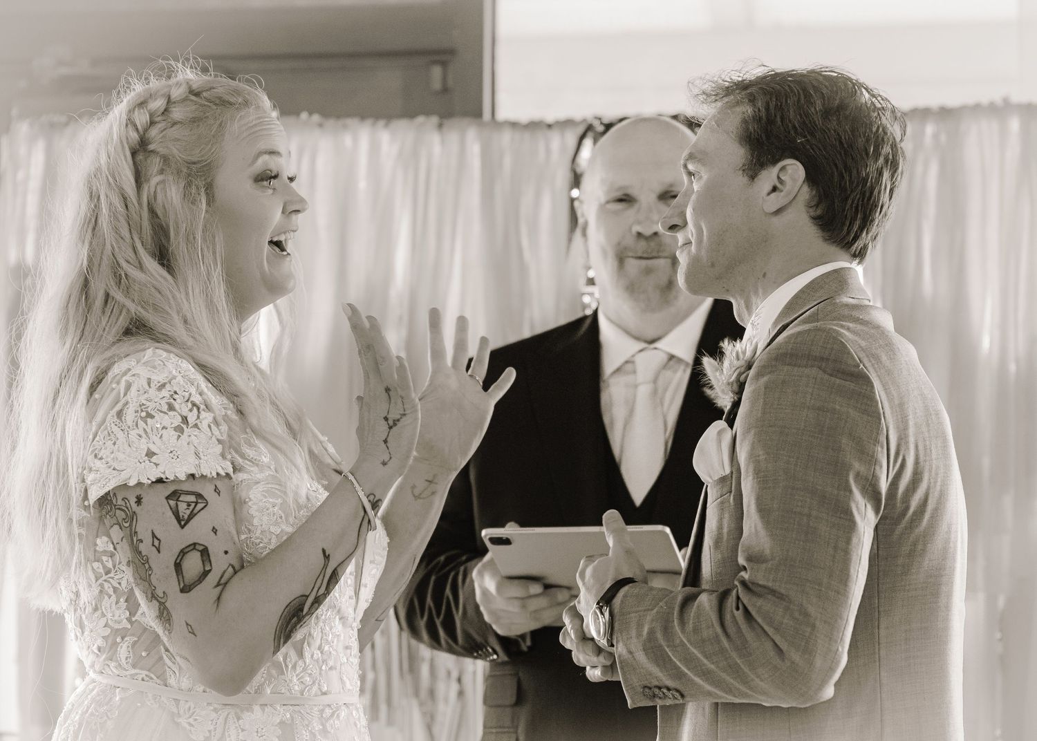 Black and white photo of a bride and groom exchanging vows with an officiant at their wedding ceremony.