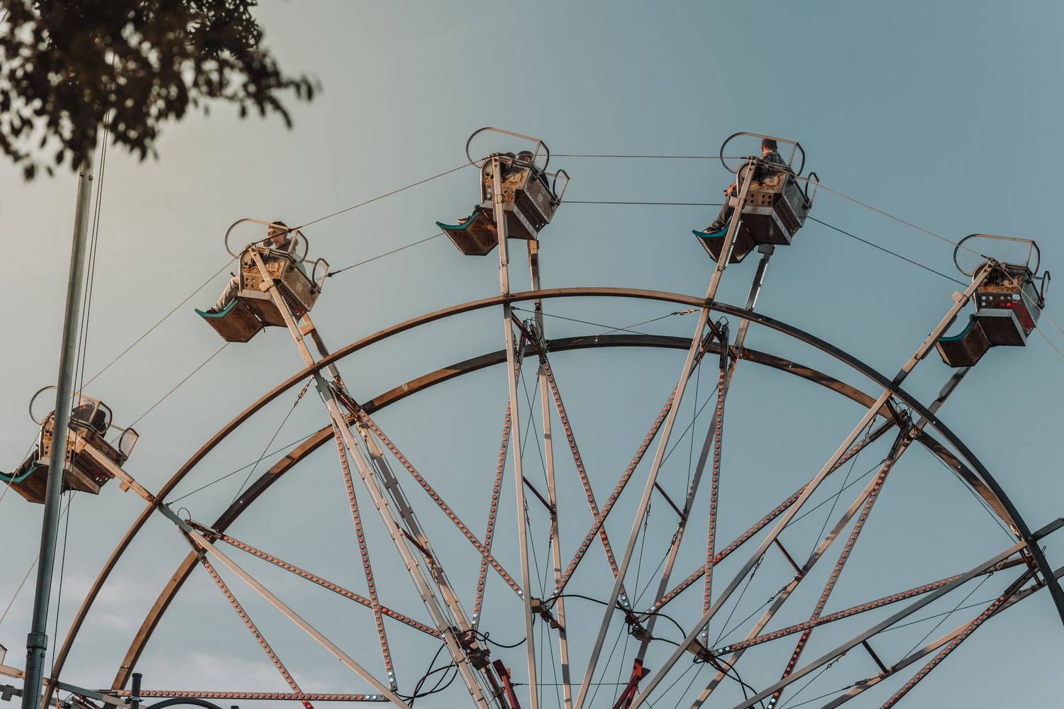 Silhouettes of chair lift seats on a ferris wheel against a cloudy blue sky at an amusement park.