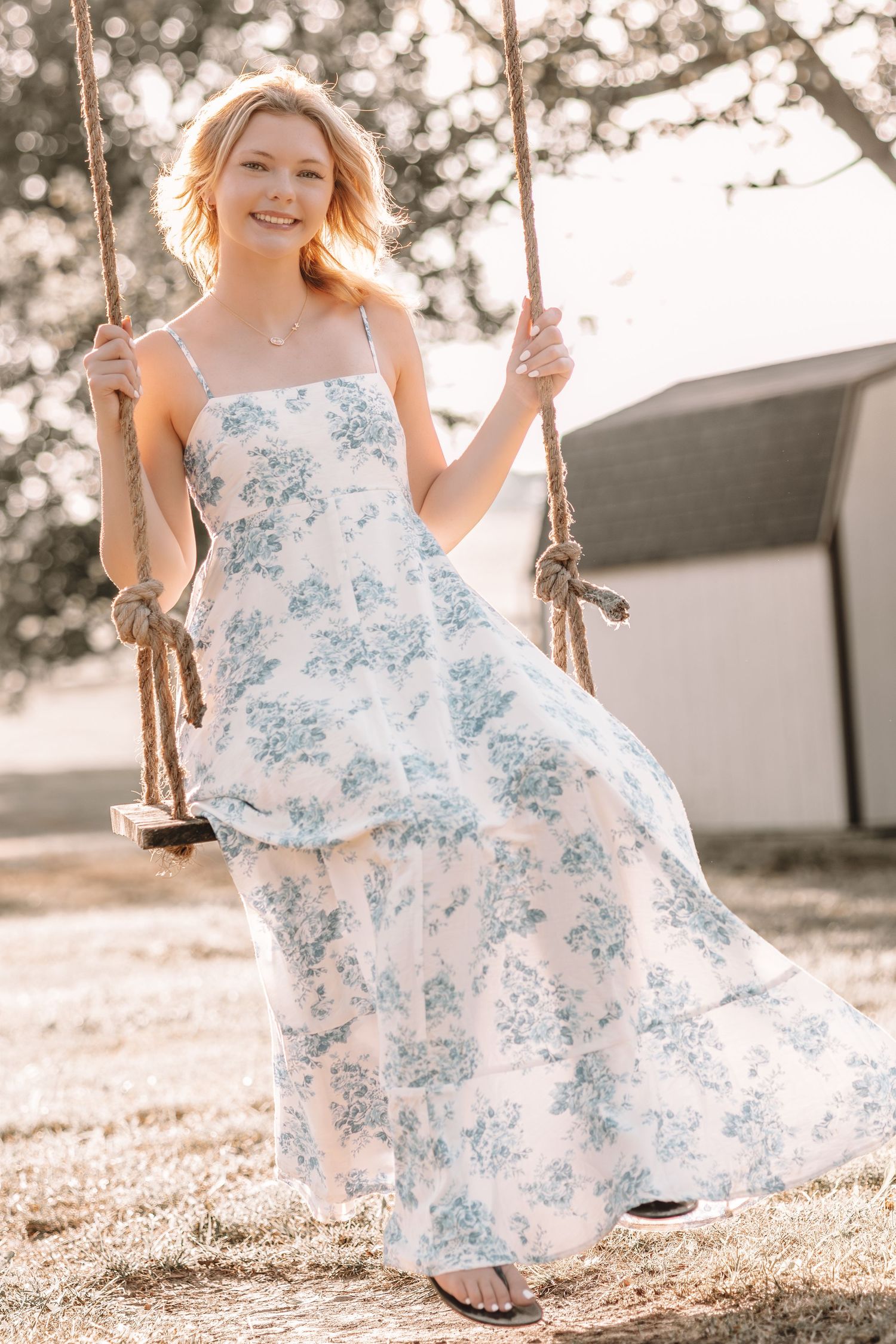A flowing white and blue floral dress catches sunlight while swinging in a pastoral setting.