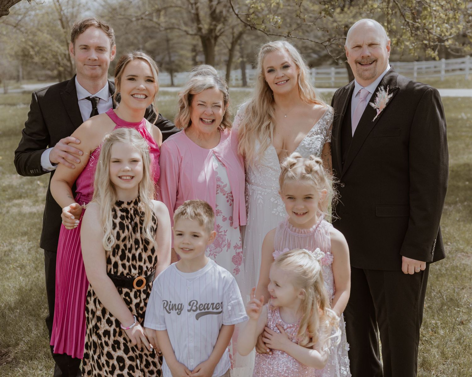 Large family group photo at a wedding outdoors, featuring bride in white gown surrounded by adults and children.