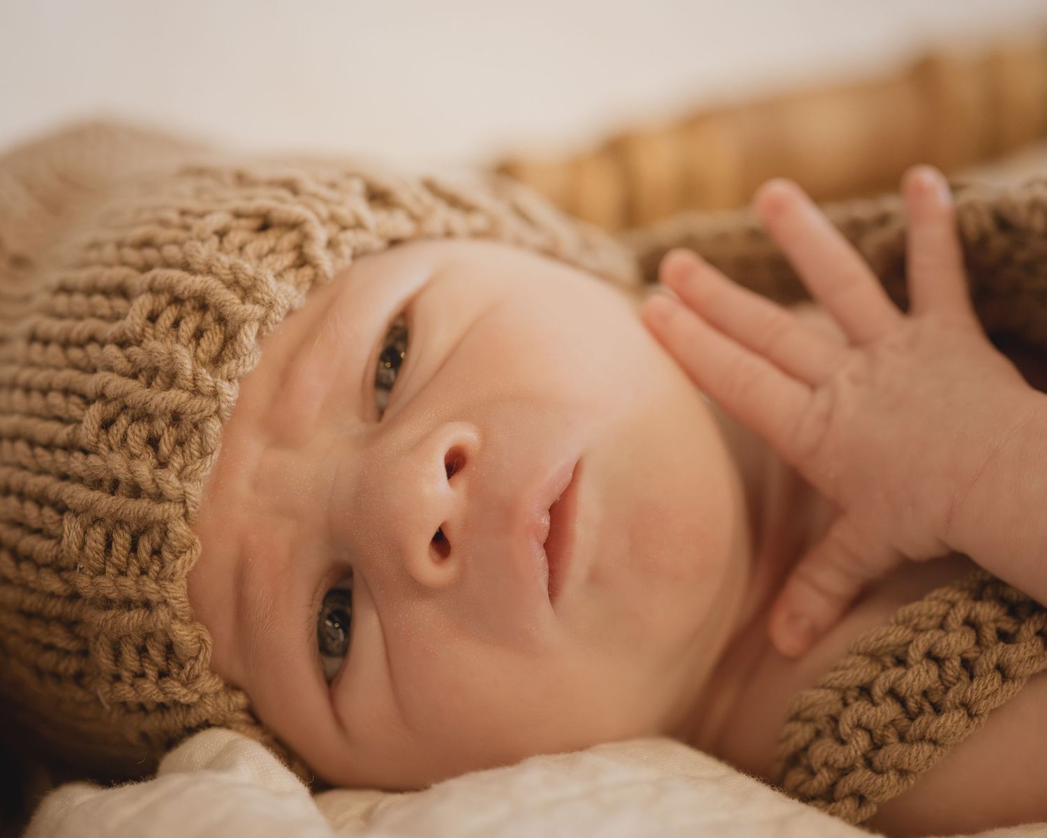 Adorable newborn baby wearing a cozy knit brown hat and outfit, lying in a basket with bright blue eyes.