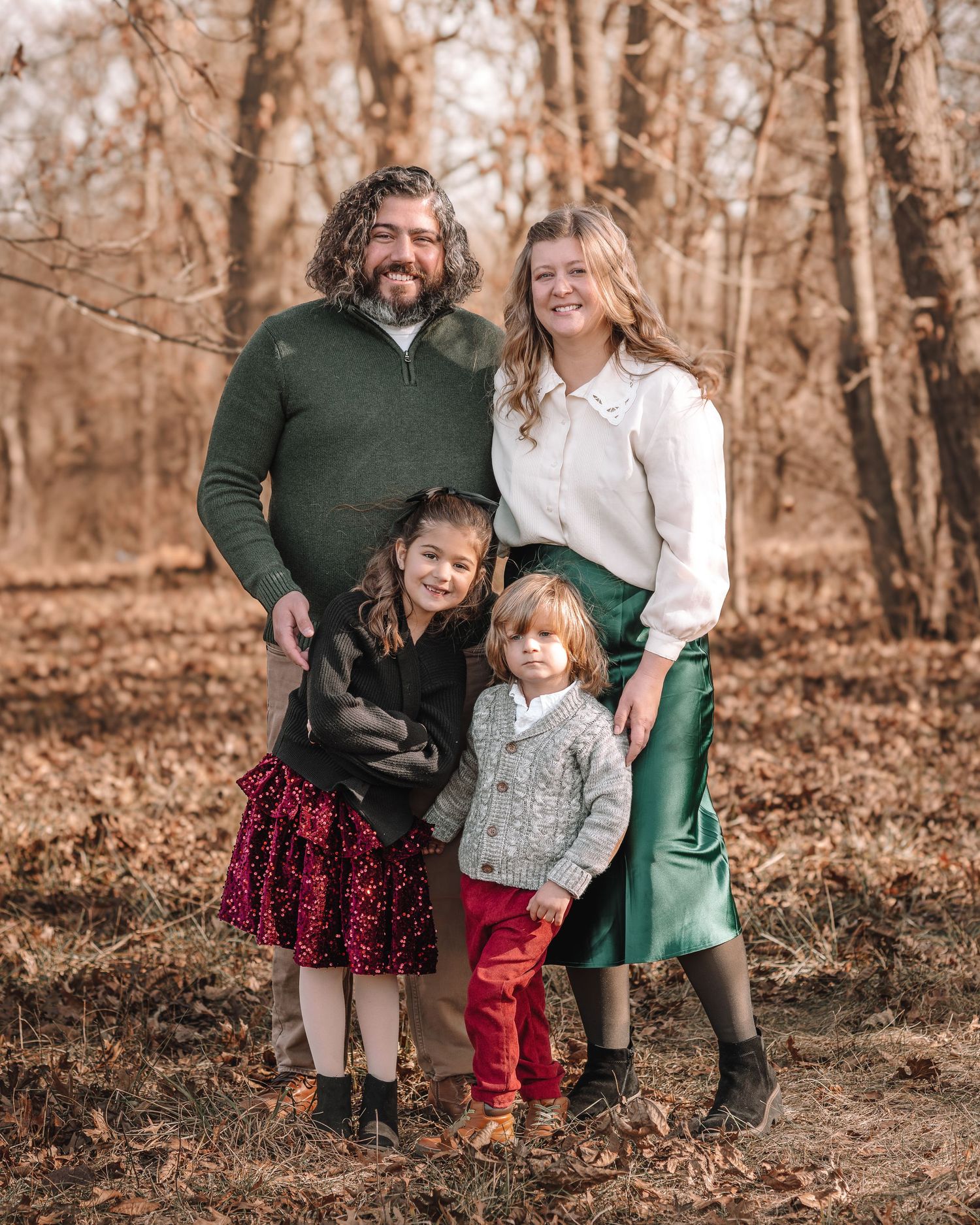 A casual outdoor family photo session in an autumn forest with coordinated burgundy and green outfits.