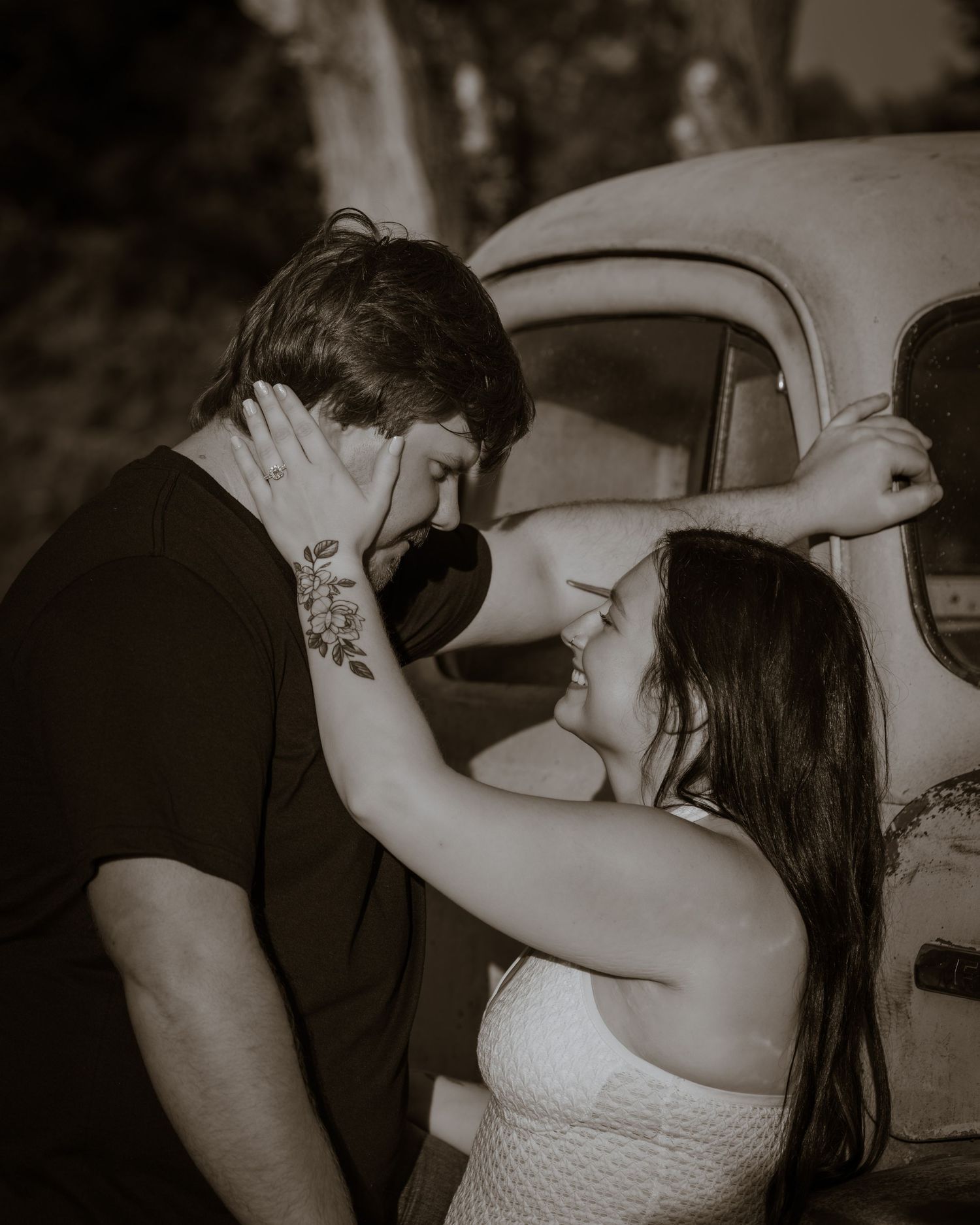 Black and white romantic couple nearly kissing beside vintage truck during outdoor engagement session.