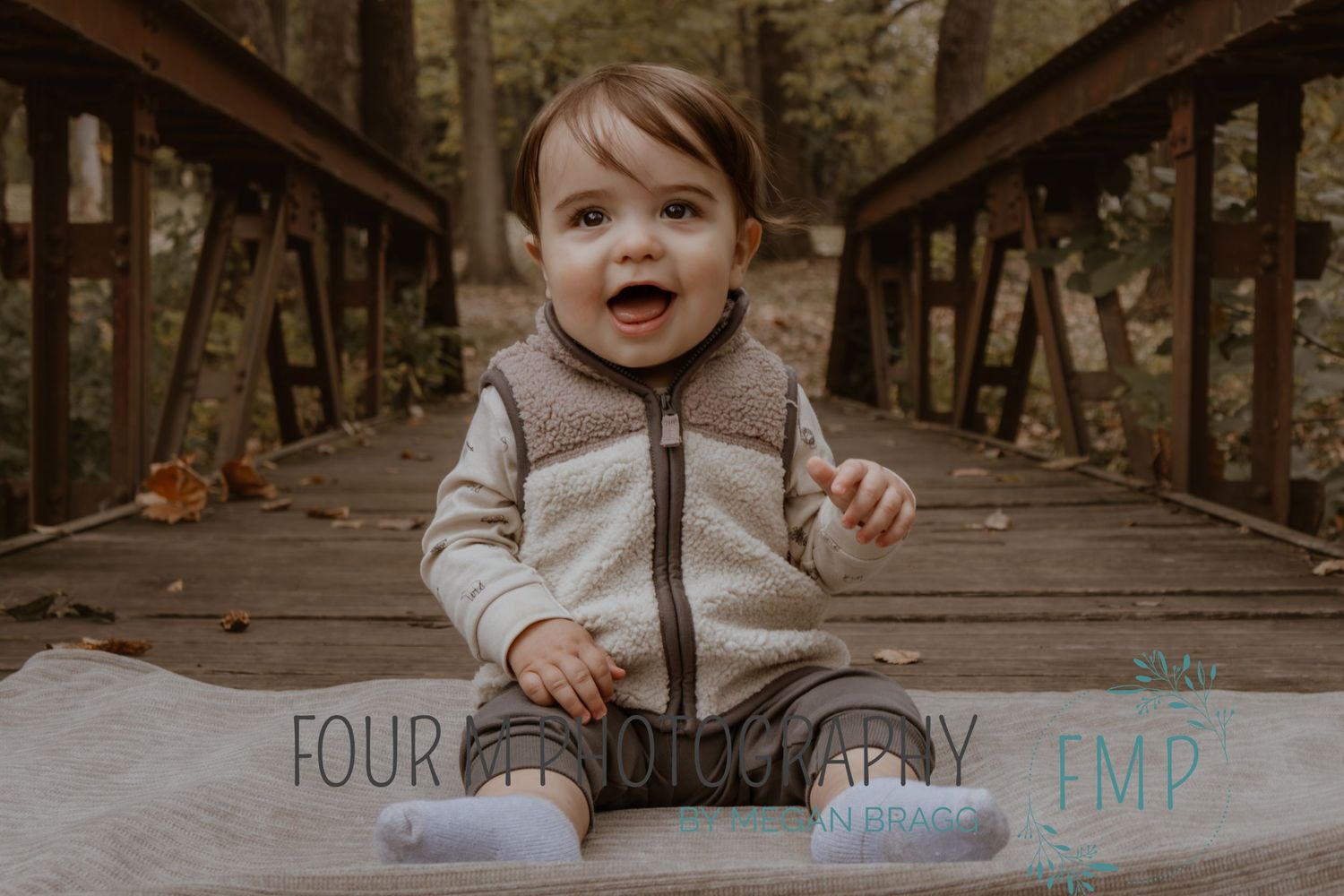 A small child walks across a wooden bridge in an autumn forest wearing a cream colored sweater and dark pants.