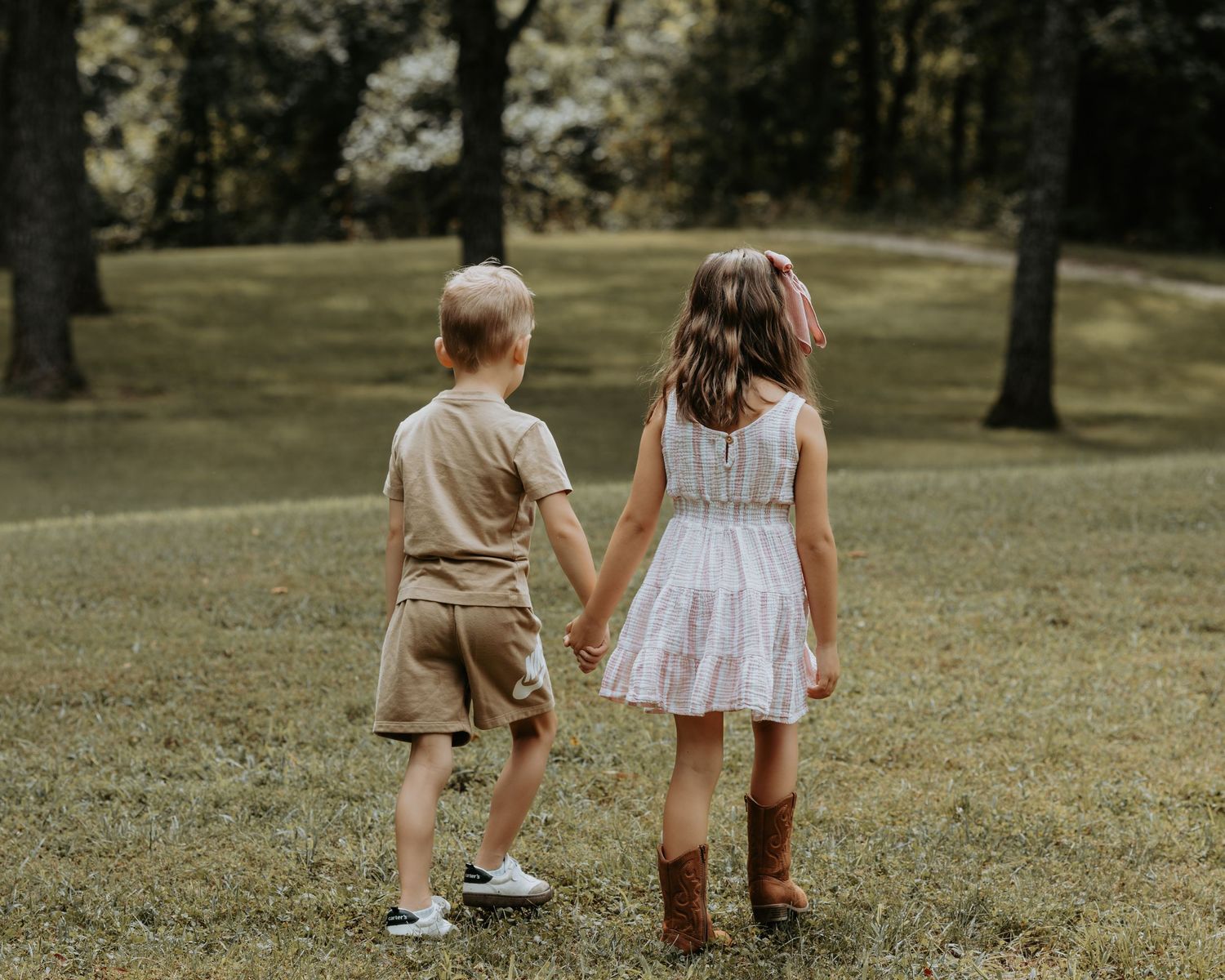 Children in summer outfits walk together across a grassy lawn on a warm afternoon.