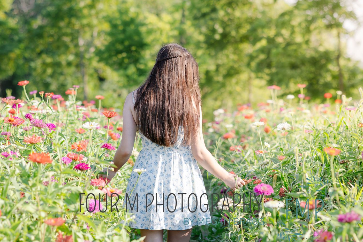 A person in a blue dress walks through a vibrant garden filled with pink and red zinnias on a sunny summer day.