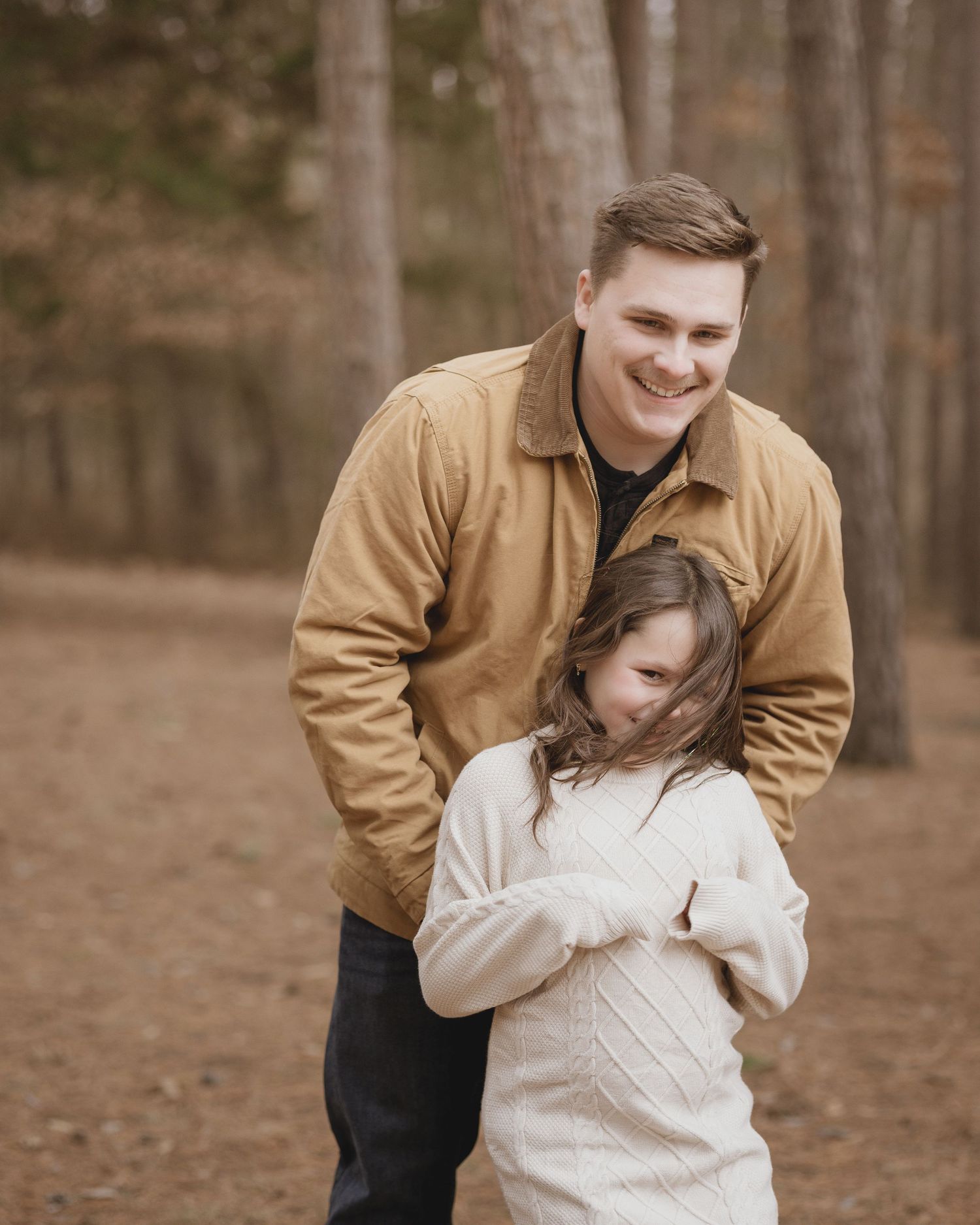 Playful outdoor photoshoot on a fall day with a couple wearing brown and cream colors in a wooded setting.