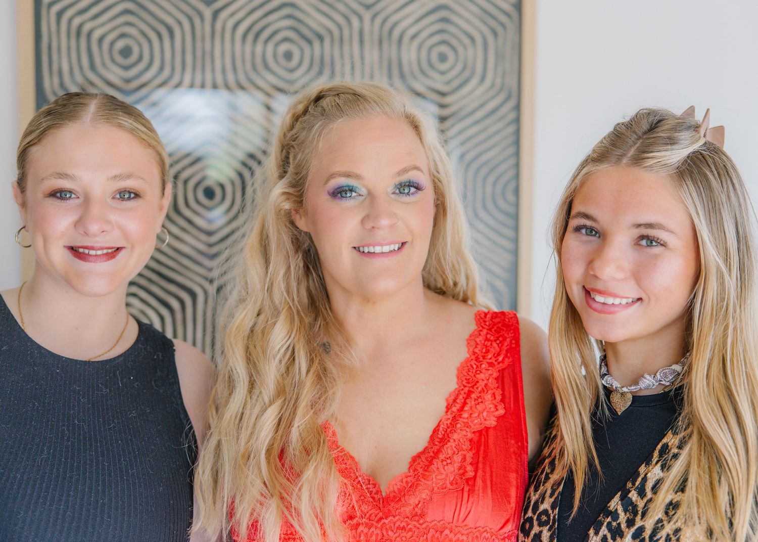 Three smiling blonde women posing together at a wedding celebration event.