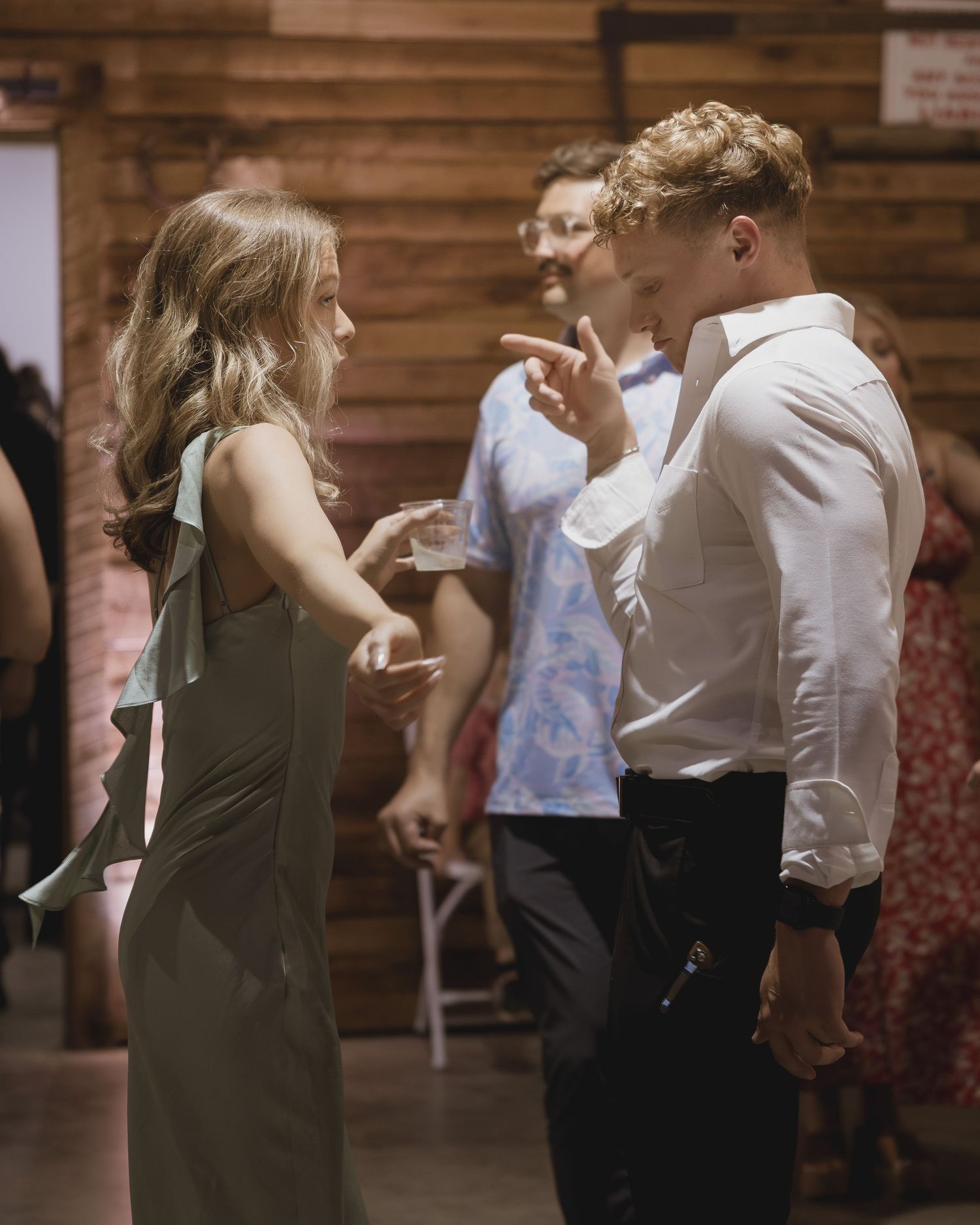 Young couple dancing and talking at a rustic barn wedding reception with guests in the background.