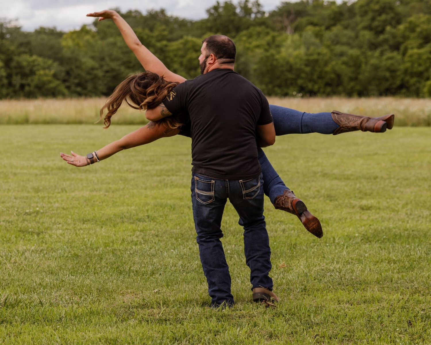 Man playfully lifting a woman like an airplane pose in an open grassy field outdoors.