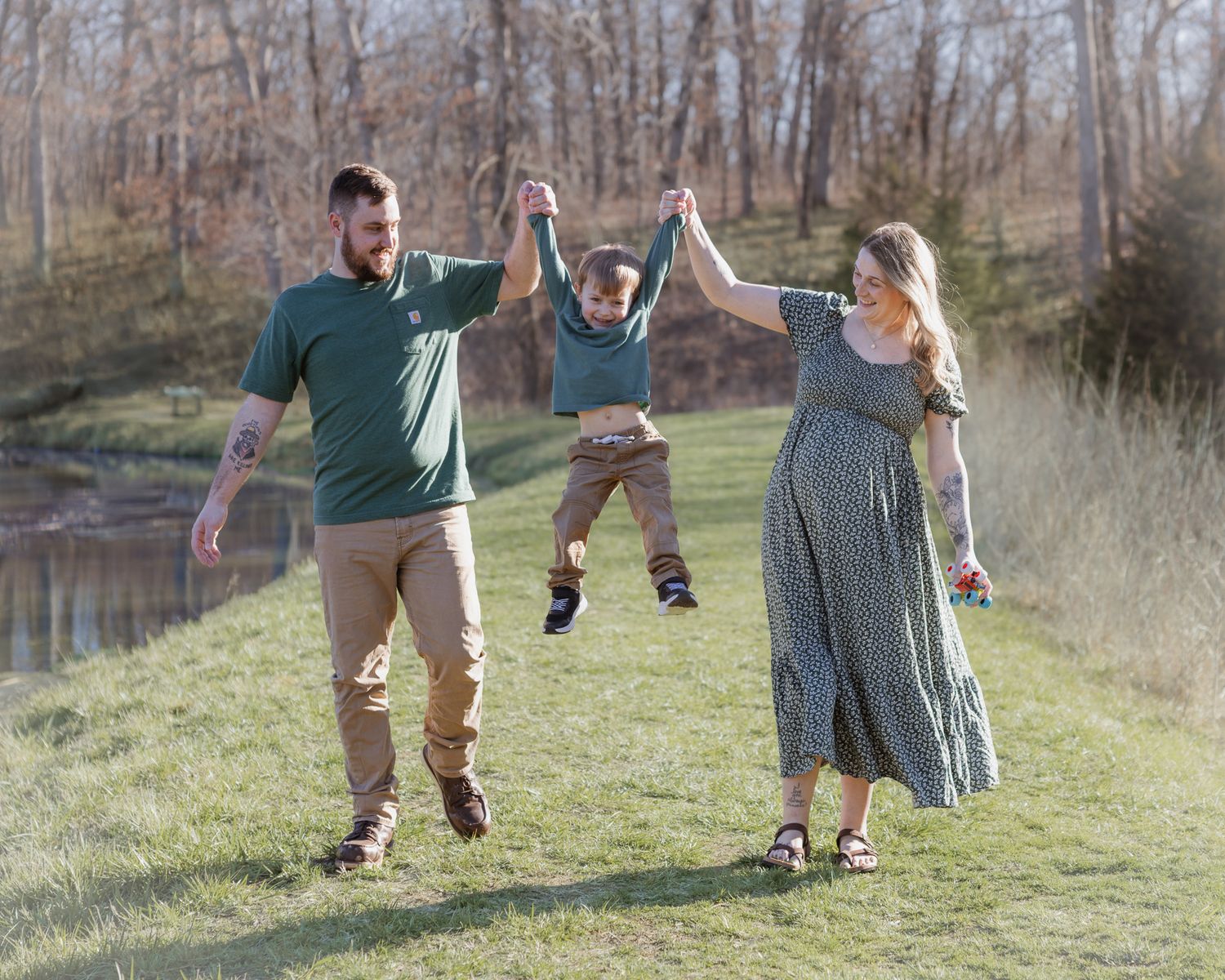 Family members hold hands and swing a child playfully between them while walking in a grassy field.