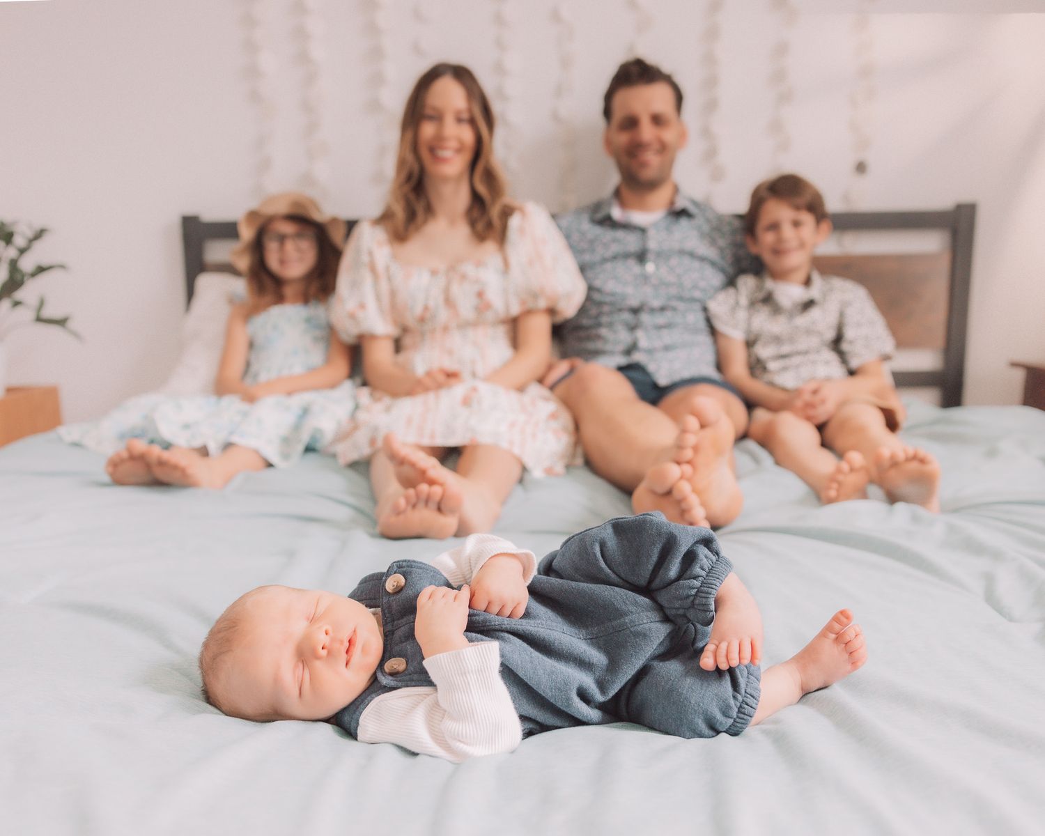 Family of five sits on a bed with newborn baby lying in the foreground.