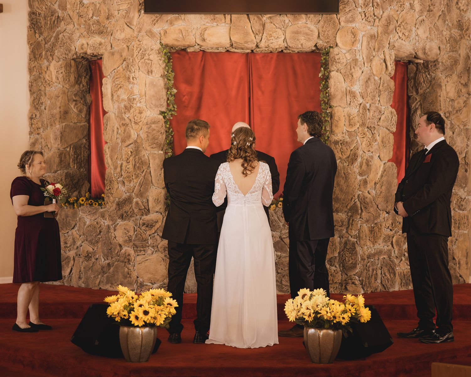 Wedding ceremony setup with stone walls, red backdrop, and yellow flower arrangements at the altar.