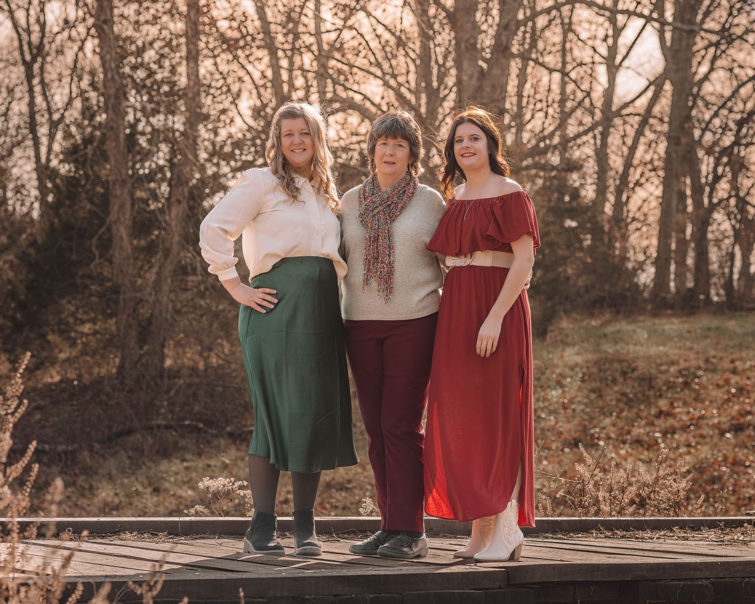 Three people in coordinating outfits pose together outdoors during a fall photo session at sunset.