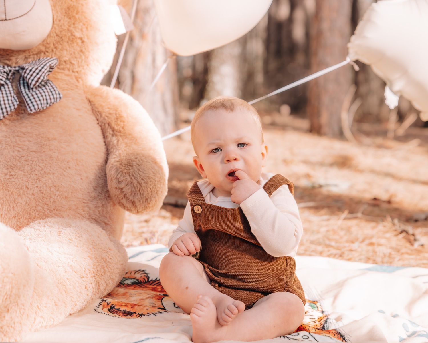 A baby plays with a brown teddy bear on a soft blanket in warm sepia tones.
