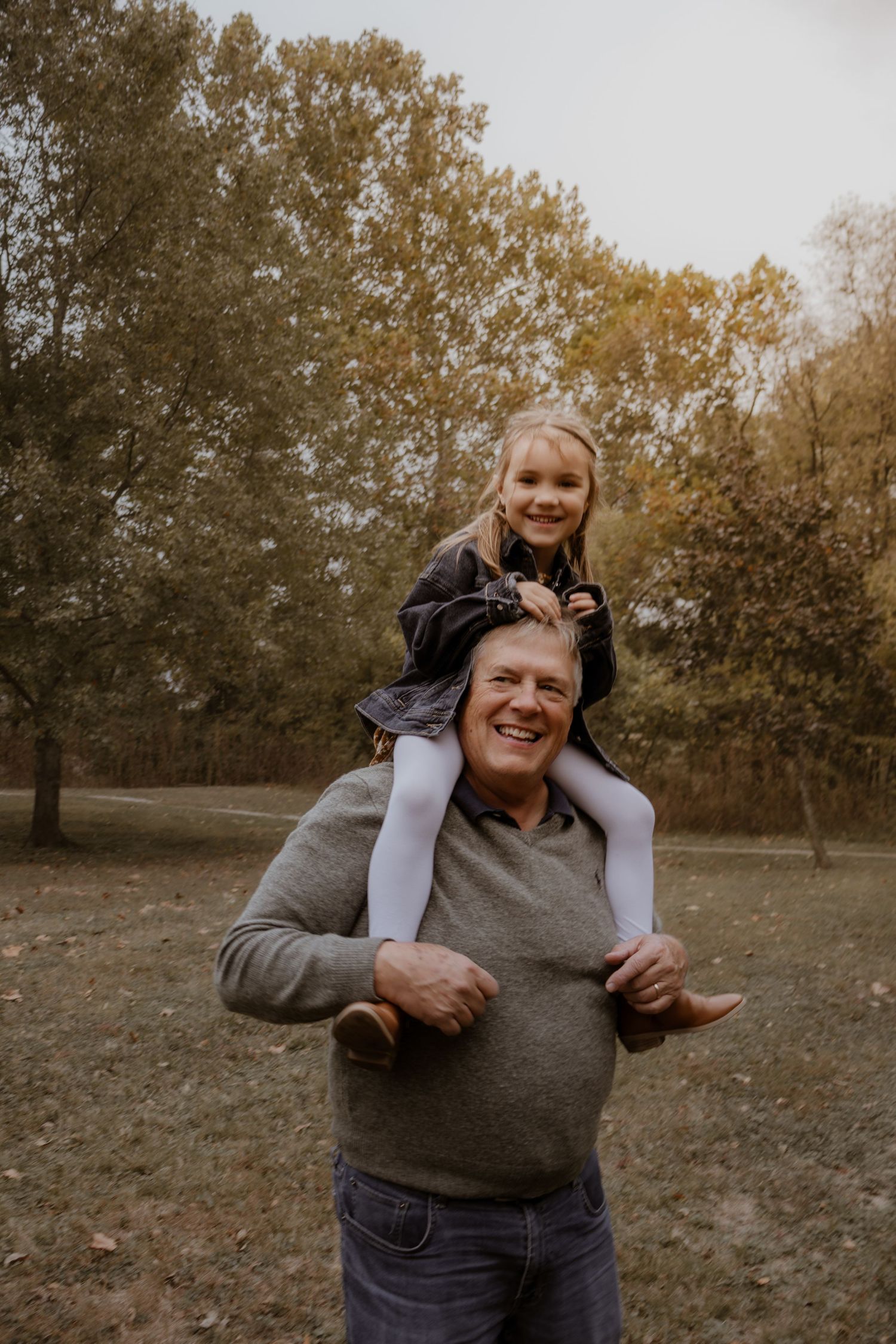 A playful moment captured in autumn showing joyful interaction between family members in a park setting.