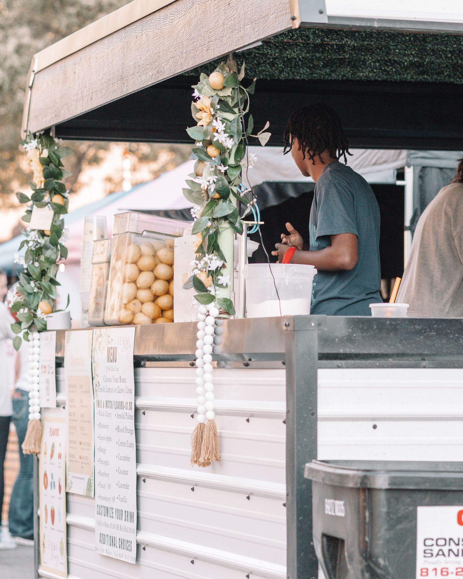 Food vendor cart decorated with greenery vines selling snacks at an outdoor market.