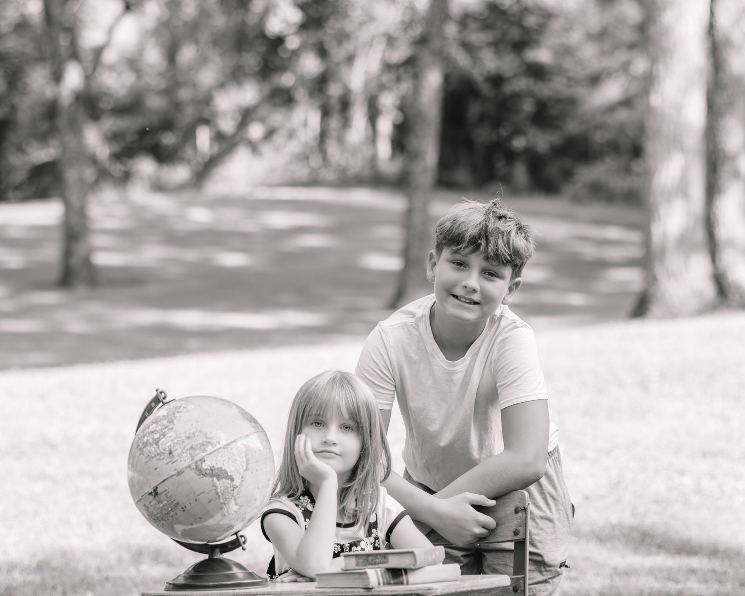 Two children lie on grass reading books together in a peaceful outdoor setting.