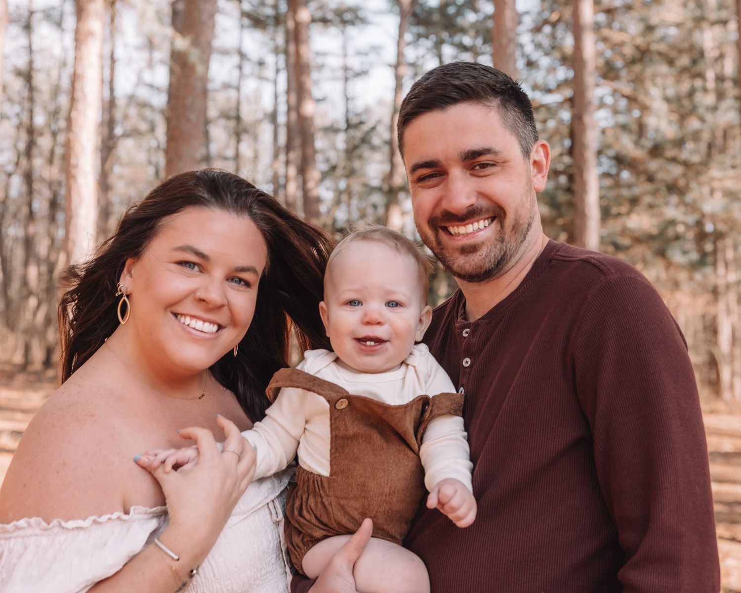 A family shares tender moments together during an outdoor photo session in a sunlit pine forest.