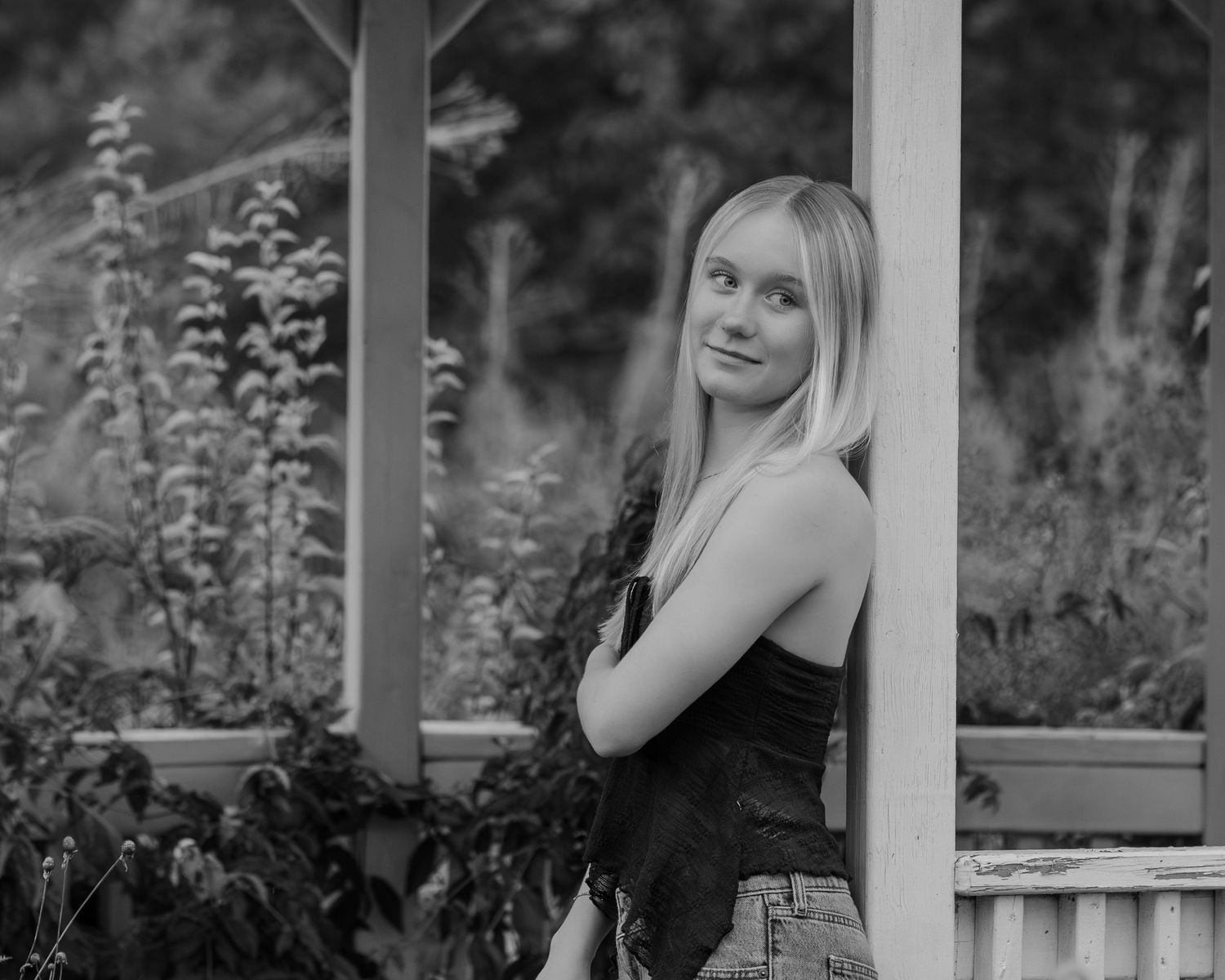 A black and white portrait series showing different poses of someone sitting on a porch railing near flowering plants.