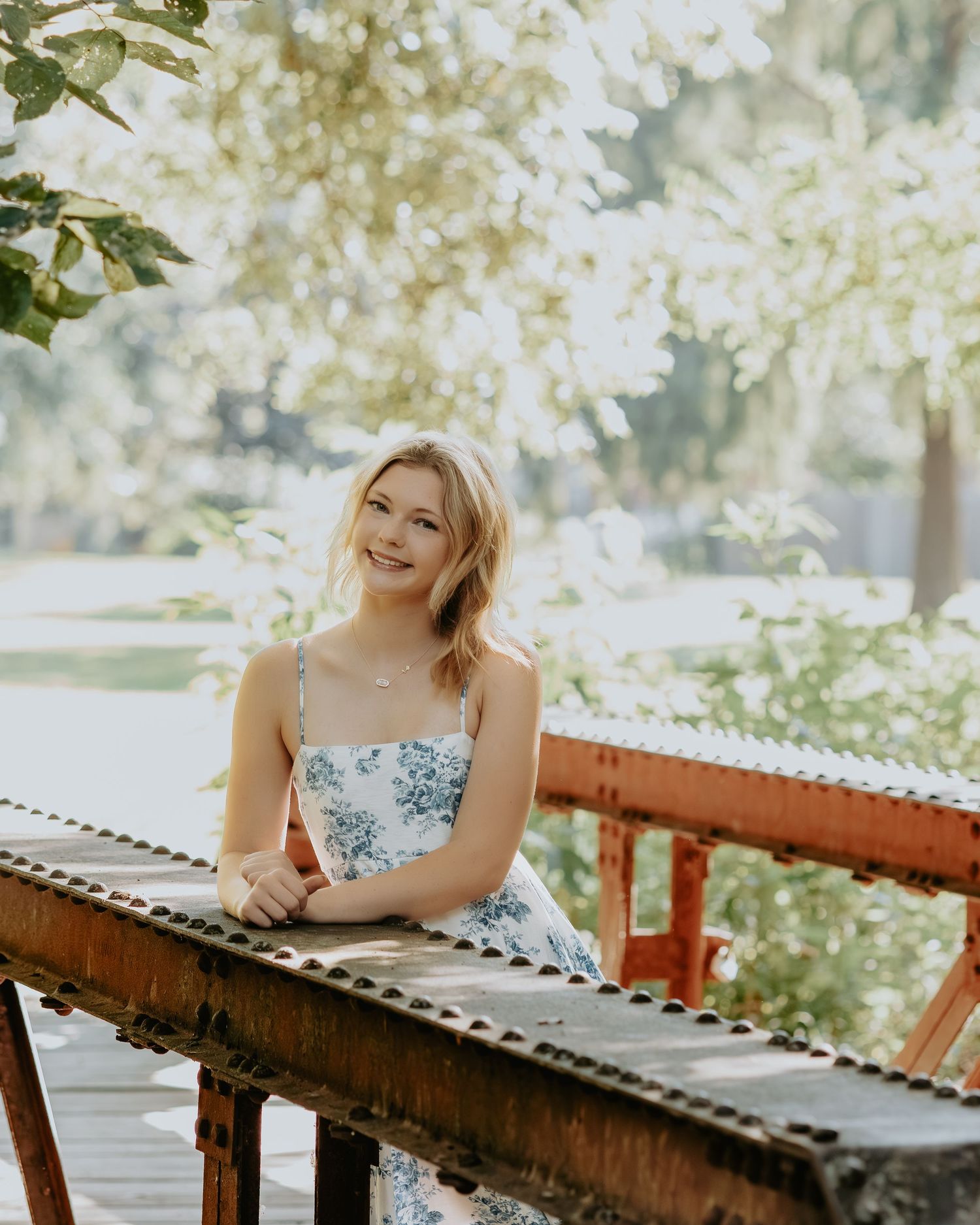 Person in floral dress relaxing on a wooden deck in dappled sunlight.